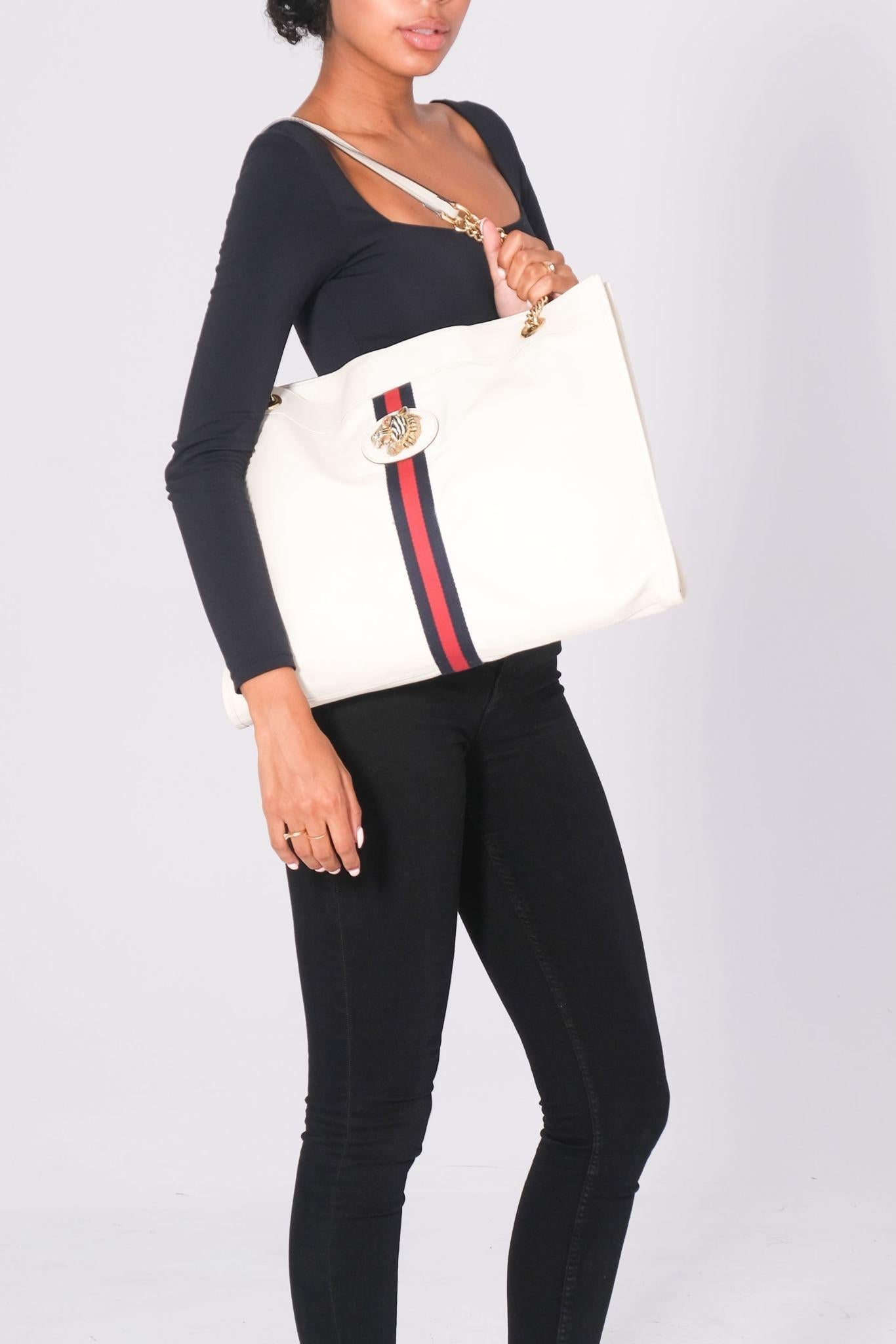 This Gucci tote by Alessandro Michele is constructed of neutrals leather, featuring the signature Sylvie Web accent and Rajah detail. The bag showcases gold-tone hardware, chain-link shoulder straps, crystal tiger head and chain-link accents. The