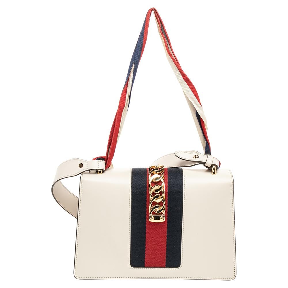 Gucci's Sylvie bag brings House codes and high-grade materials with a contemporary design. This small Sylvie is crafted using white leather and styled with a chain-Web decorated flap and a buckle lock to secure the Alcantara interior. The bag is