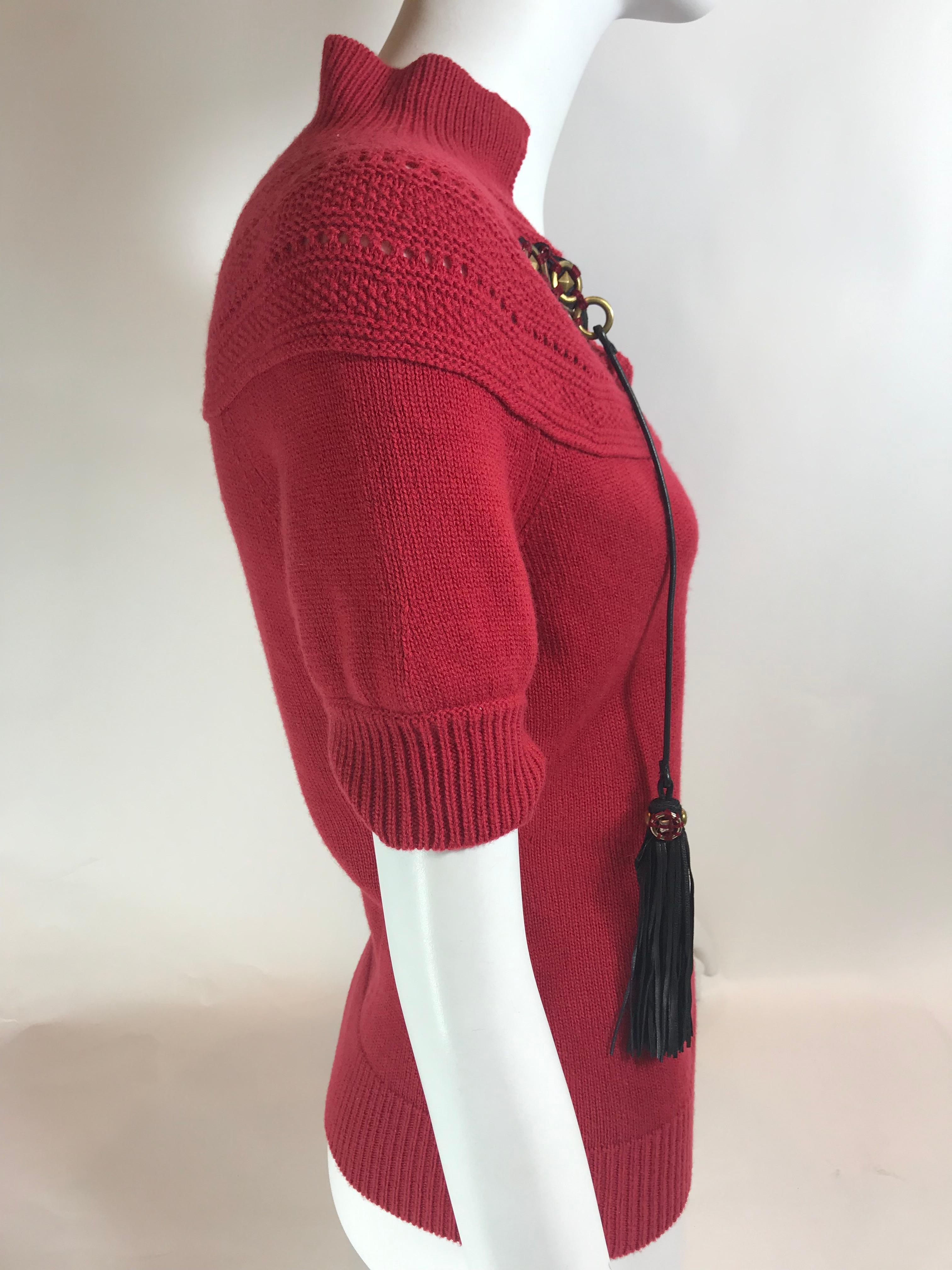 Red wool sweater with pointed collar, embellished tie closure at front featuring tassels. Short sleeves.