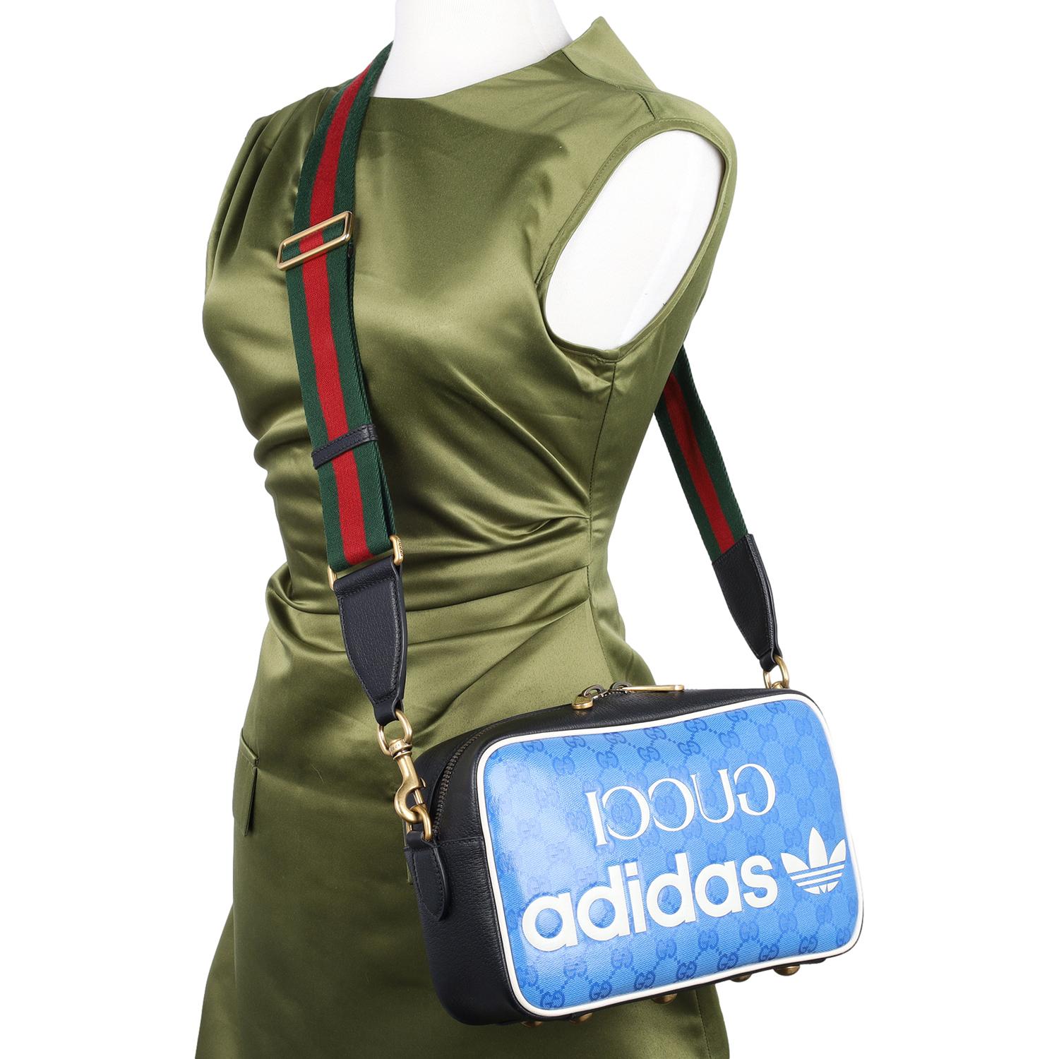 This authentic Gucci x Adidas Crystal Vintage Monogram Small Messenger Bag is a bold fusion of luxury and sporty sophistication. Designed in a striking combination of bright splash blue, off-white, and black, this standout piece is crafted from