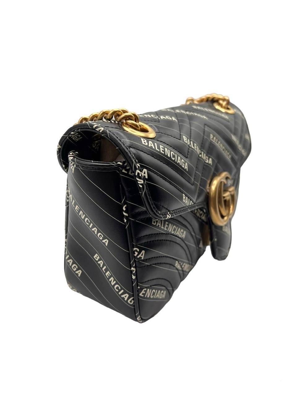 Borsa firmata Gucci in un’iconica collaborazione con il brand Balenciaga, linea Marmont nella misura 26, realizzata in pelle nera con hardware oro. Munita di una patta frontale con chiusura ad incastro. Dotata di una tracolla in catena oro e nera a