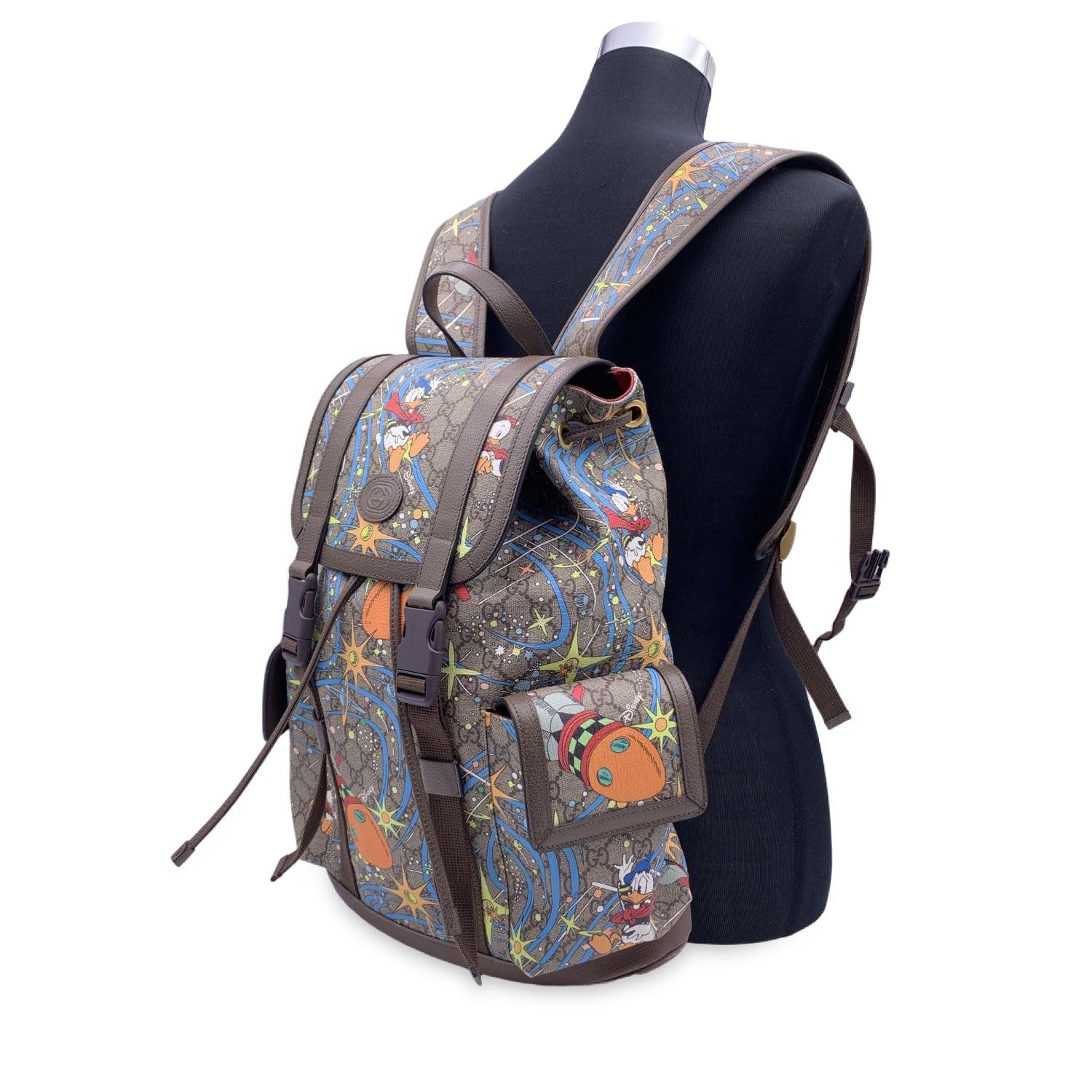 GUCCI x Disney GG Monogram canvas Donald Duck Backpack. It is crafted in GG supreme monogram canvas with multicolor Donald Duck and rocket print and brown leather trim. The bag has a flap top with double buckle, drawstring closure and 2 front flap