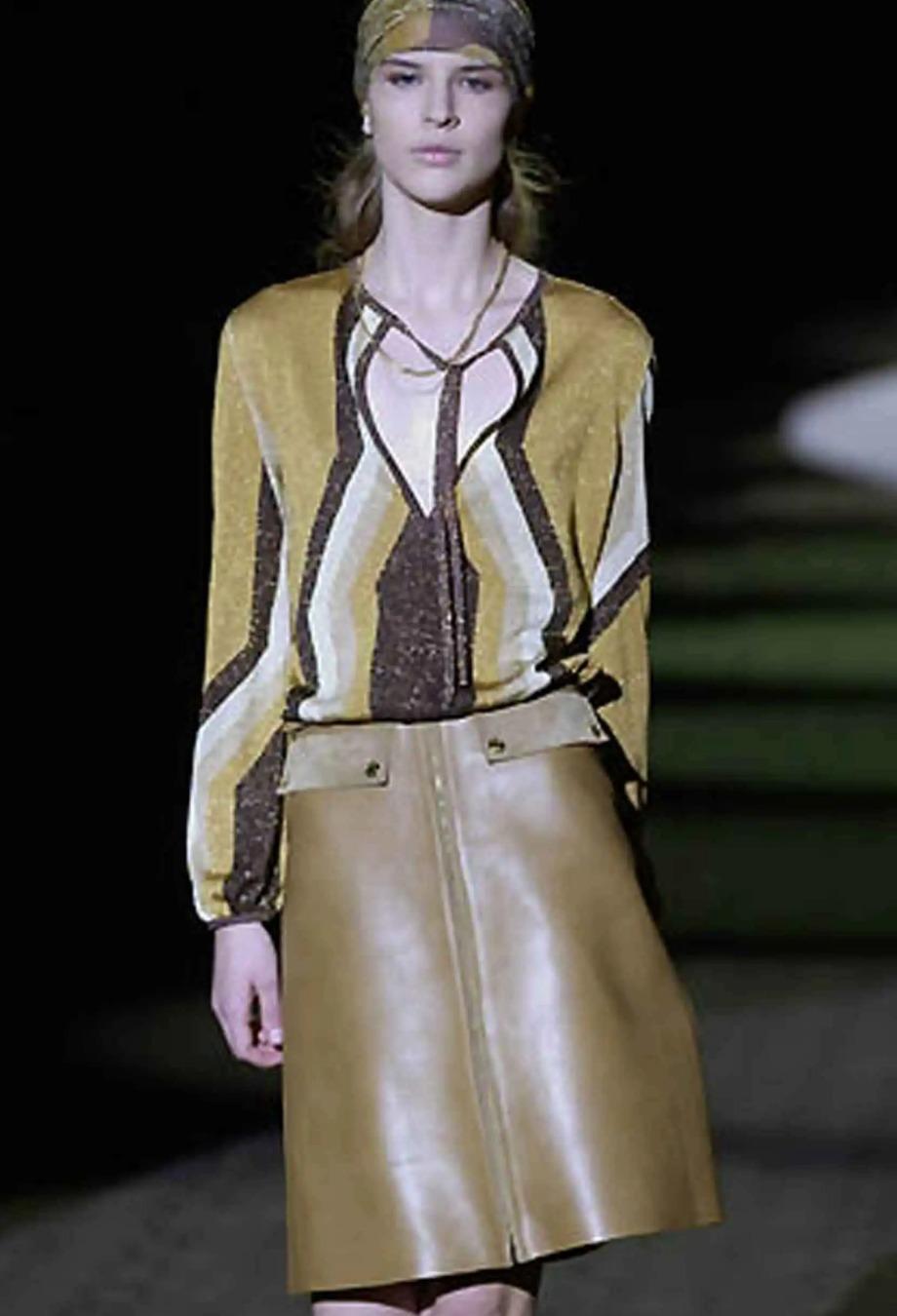 Debuttato in passerella, questo capo della collezione A. Winter 2000 di Gucci è realizzato in maglia metallica scintillante con una scollatura a buco di serratura accentuata da una delicata cravatta. Le strisce grafiche chevron in oro brunito, nero