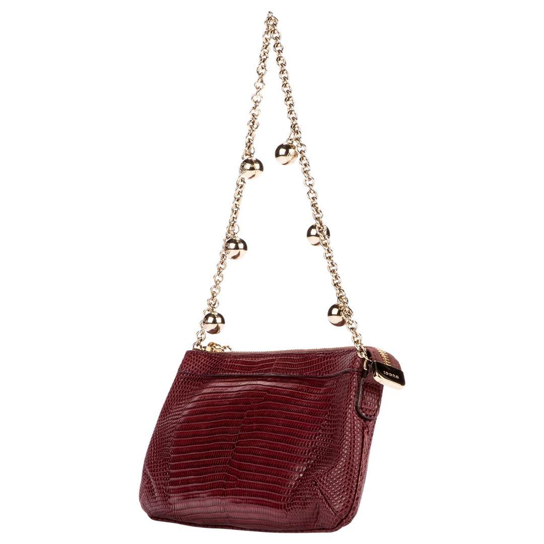 Yet another iconic creation from a Gucci x Tom Ford collaboration! Rendered in a beautiful burgundy lizard leather with gold hardware and a single gold chain strap with decorative gold Gucci balls. The zipper closure opens to a burgundy GG logo