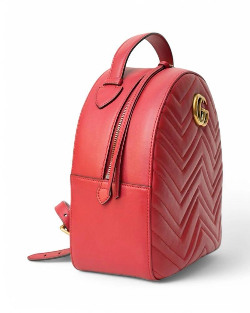 Sac à dos signé Gucci, ligne Marmont, en cuir matelassé rouge avec ferrures dorées. Doté d'une fermeture à glissière semi-circulaire à double curseur, doublé à l'intérieur d'un tissu en daim beige avec des poches pratiques, le sac à dos est assez