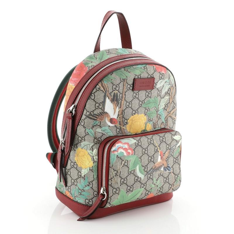 This Gucci Zip Pocket Backpack Tian Print GG Coated Canvas Small, crafted from brown GG supreme coated canvas overlaid with Tian print, features adjustable web shoulder straps, top handle, exterior front zip pocket and silver-tone hardware. Its zip