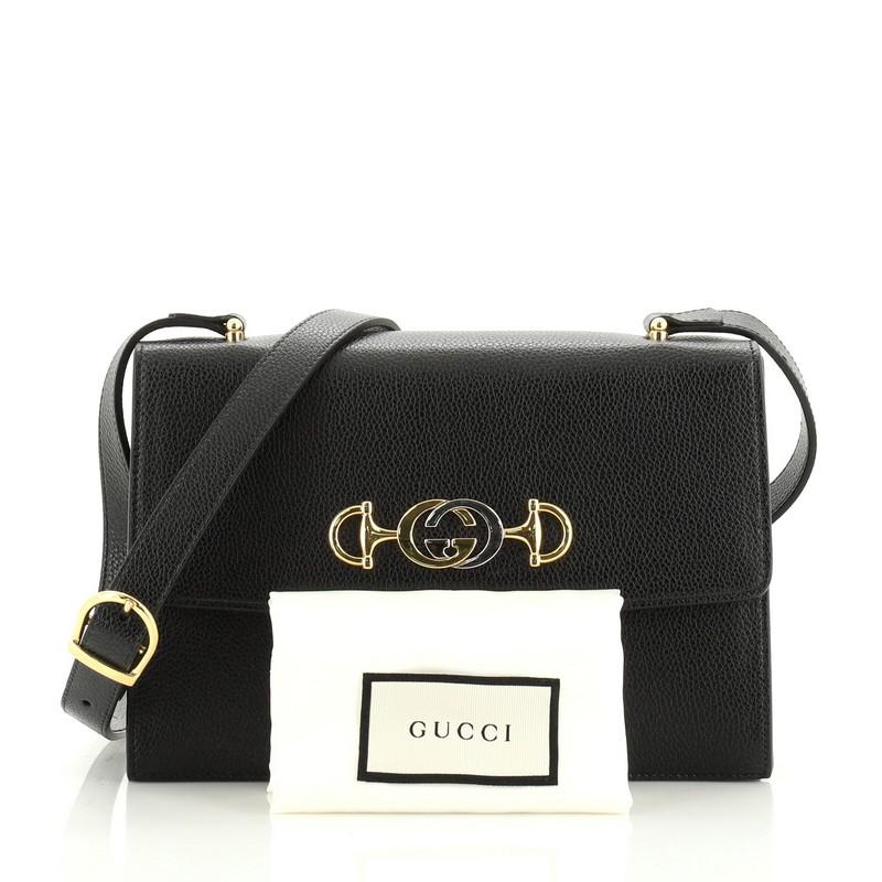 This Gucci Zumi Flap Shoulder Bag Leather Small, crafted in black leather, features an adjustable leather strap, interlocking G Horsebit detail, and gold-tone hardware. Its flap opens to a red fabric interior with three open compartments and side