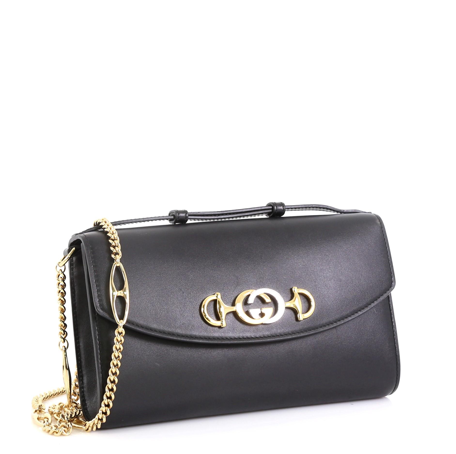 This Gucci Zumi Shoulder Bag Leather Small, crafted in black leather, features adjustable leather handles, Marina chain shoulder strap, interlocking G Horsebit, and gold-tone hardware. Its magnetic snap closure opens to a red leather interior with