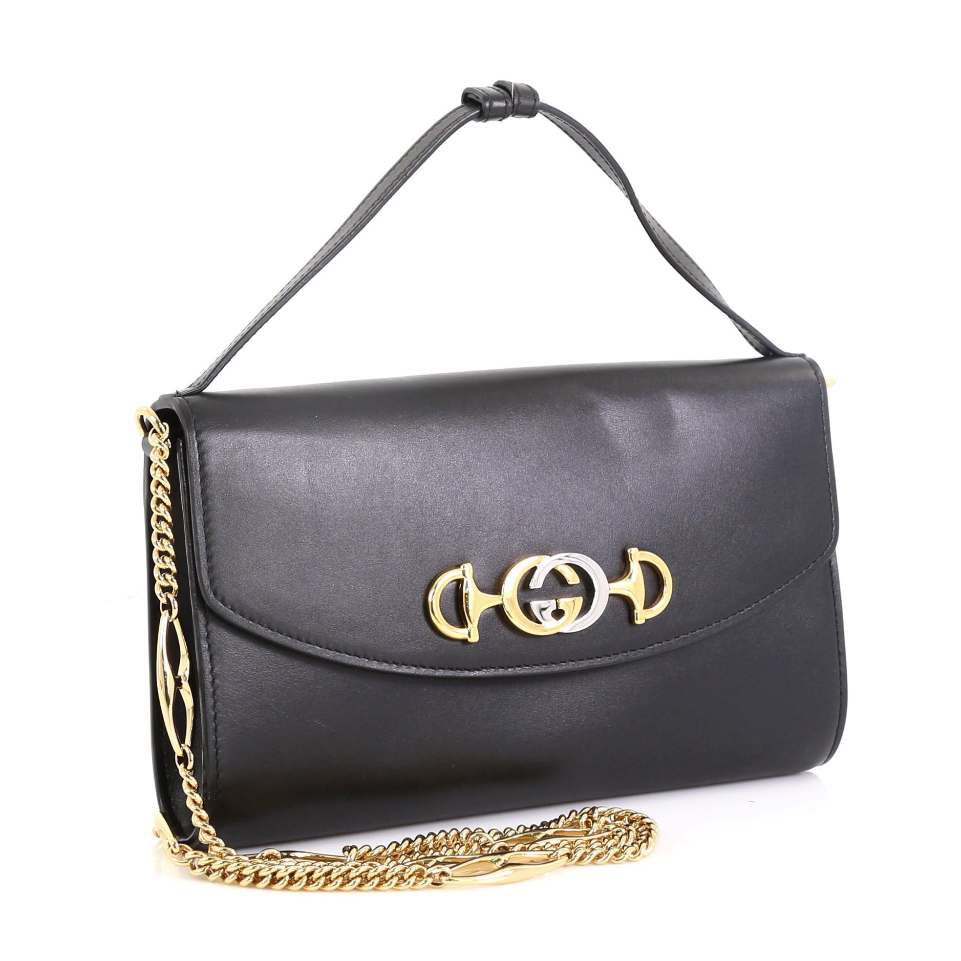 This Gucci Zumi Shoulder Bag Leather Small, crafted in black leather, features adjustable leather handle, Marina chain shoulder strap, interlocking GG Horsebit, and gold-tone hardware. Its magnetic snap closure opens to a red leather interior with