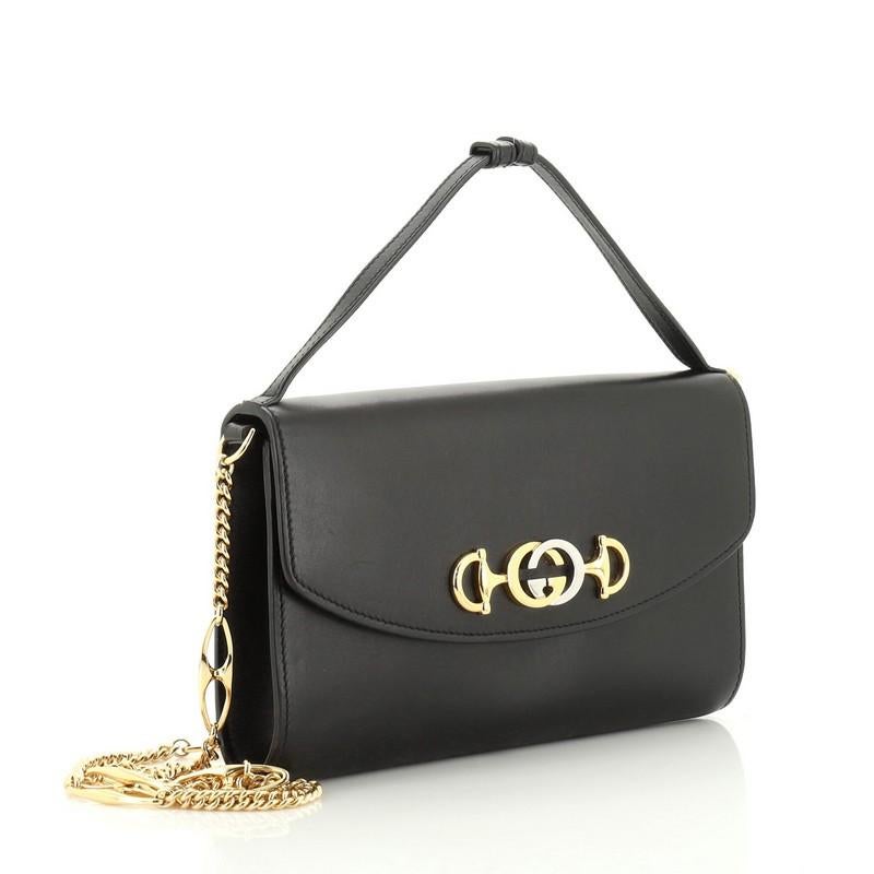 This Gucci Zumi Shoulder Bag Leather Small, crafted in black leather, features an adjustable leather handle, Marina chain shoulder strap, interlocking G Horsebit, and gold and silver-tone hardware. Its magnetic snap closure opens to a red leather