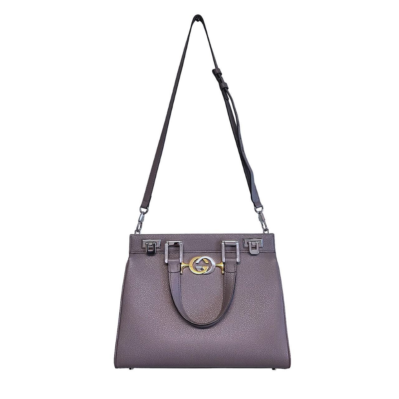 We are offering this Gucci top handle bag. Crafted in Italy, this designer bag was made with grey leather, gold-tone hardware, and silver-tone hardware. It features a silver and gold-tone Gucci GG logo and dual leather top handles. It has a