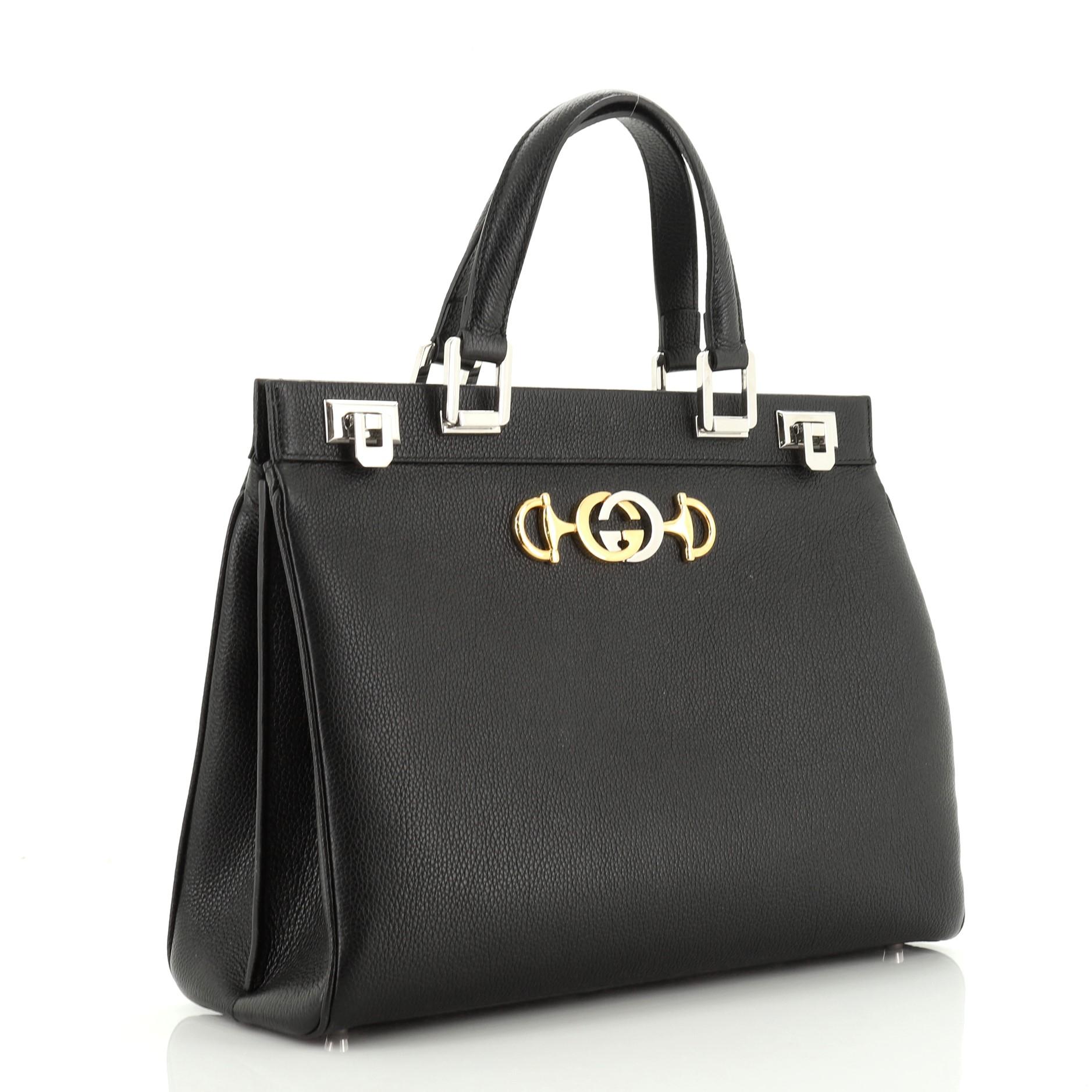 This Gucci Zumi Top Handle Bag Leather Medium, crafted in black leather, features dual leather handles, Interlocking G Horsebit detail, top frame with a hinged lock on each side and gold and silver-tone hardware. Its flip-lock closure opens to a red