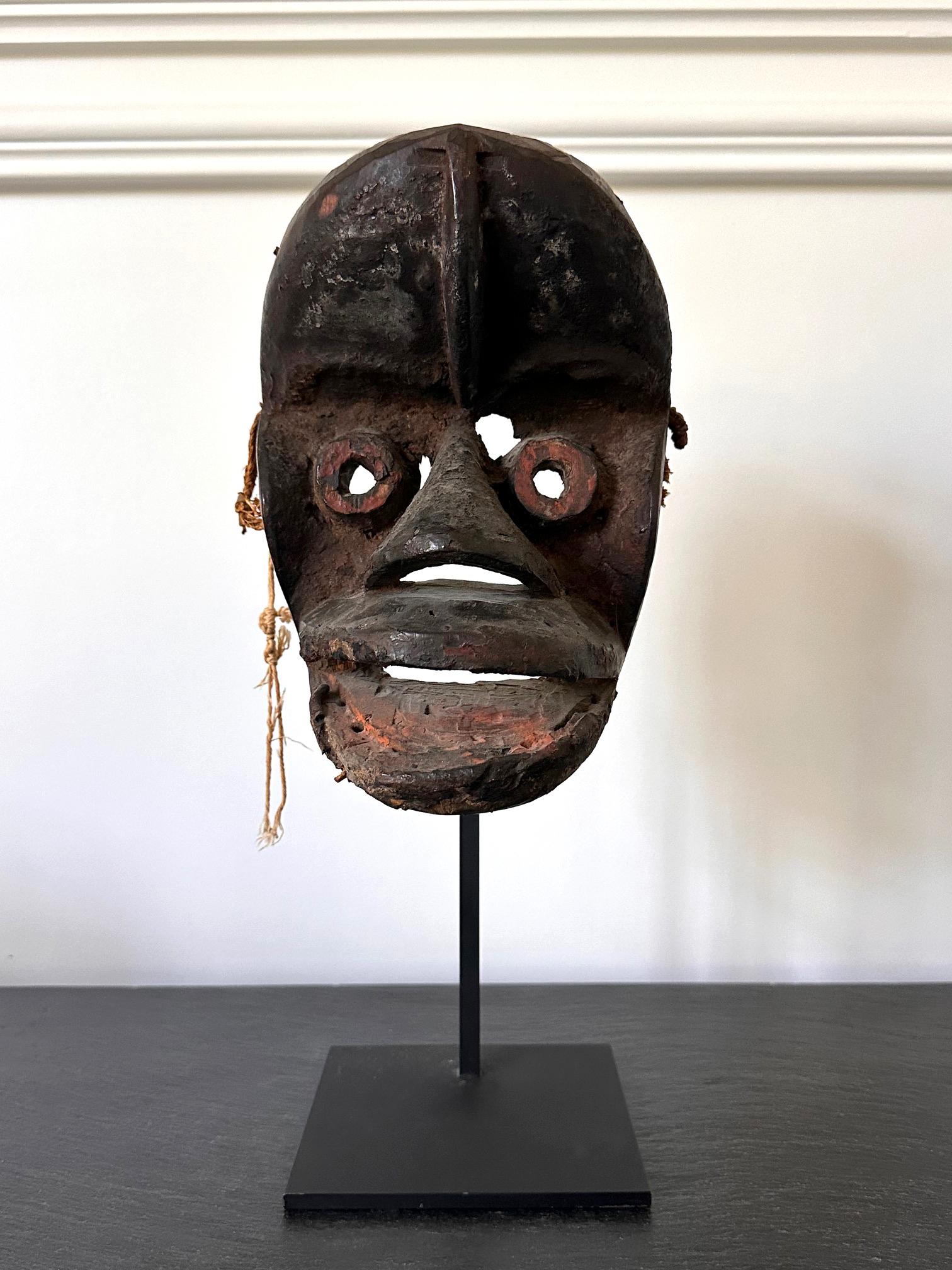 Una maschera in legno di Guere con vernice e resti di fibre di Wood people esposta su un supporto di metallo. I We (conosciuti anche come Krahn o Guere) sono un popolo africano indigeno che abita le zone dell'attuale Liberia orientale e della Costa