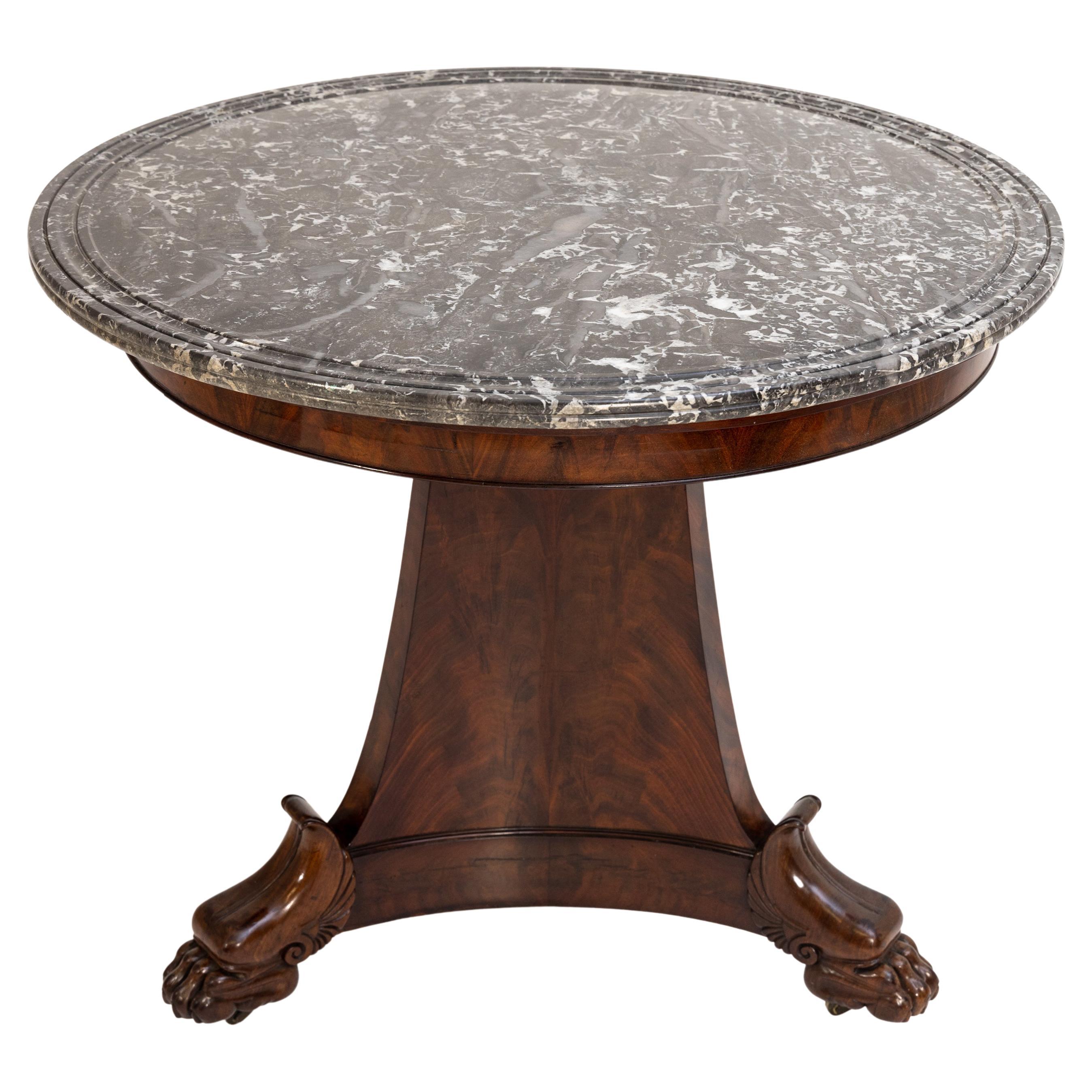 Three-legged gueridon with gray marble top and paw feet. The table stands on brass casters and is veneered in mahogany.
