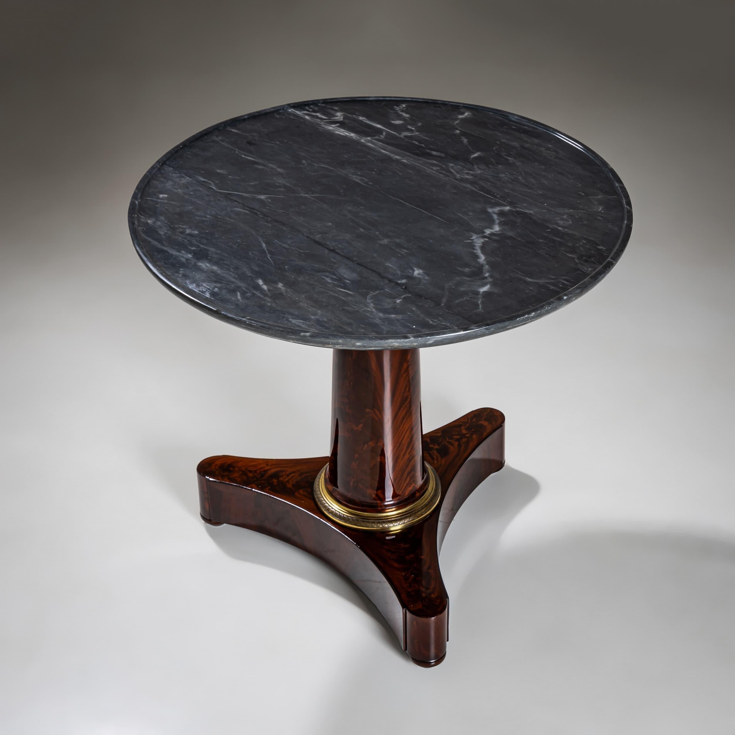 Table d'appoint ronde datant d'environ 1830, avec un plateau en marbre gris foncé. La base est en placage d'acajou avec un motif de grain saisissant. La colonne centrale, légèrement effilée, repose sur une base trilobée aux angles arrondis. Un
