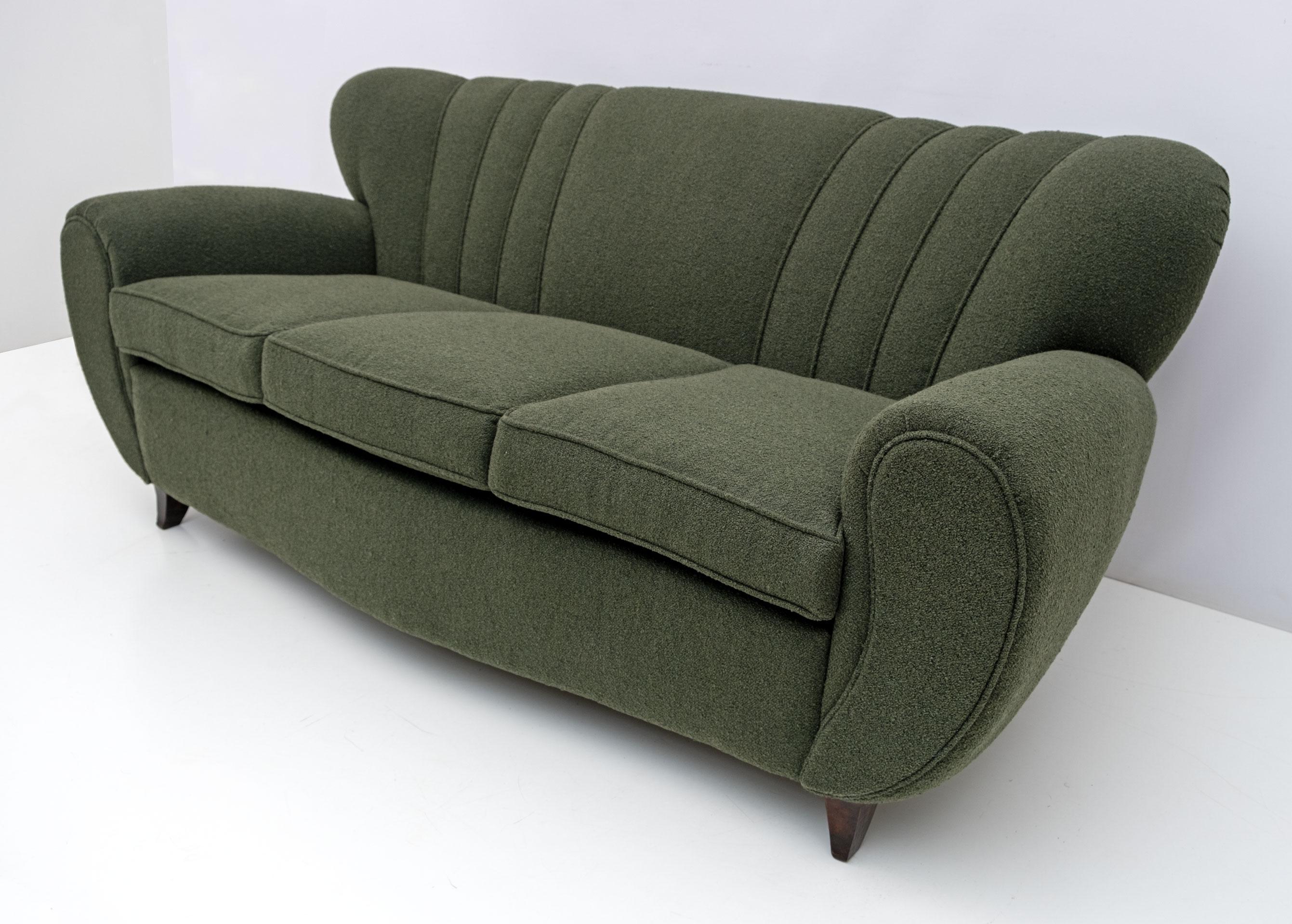 Grand canapé sculptural italien attribué à Guglielmo Ulrich, très confortable. Récemment tapissé en Bouclè vert, fini avec une bordure du tissu lui-même, afin d'accentuer ses formes courbes. Les pieds fuselés et incurvés en hêtre teinté noyer ont