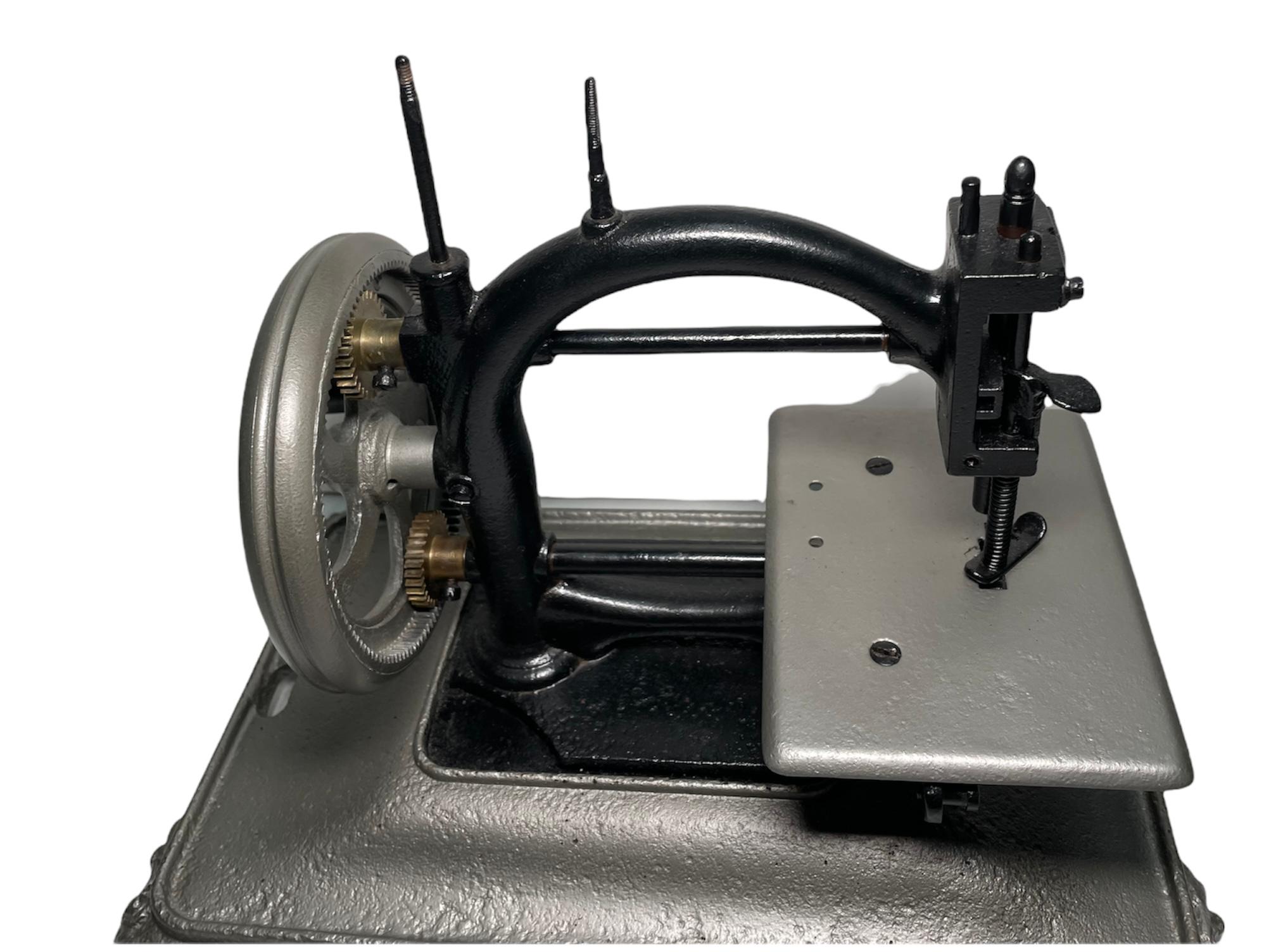 This is a Guhl & Harbeck style chainstitch hand crank sewing machine. The C shaped cast iron machine is painted black and its rectangular base with four scrolls and shells feet corner is painted silver color. The sewing machine does not work. It is