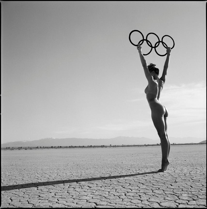 Guido Argentini Nude Photograph – Olympische Spiele – nacktes Modell in der Wüste, das die Olympischen Ringe hoch hält