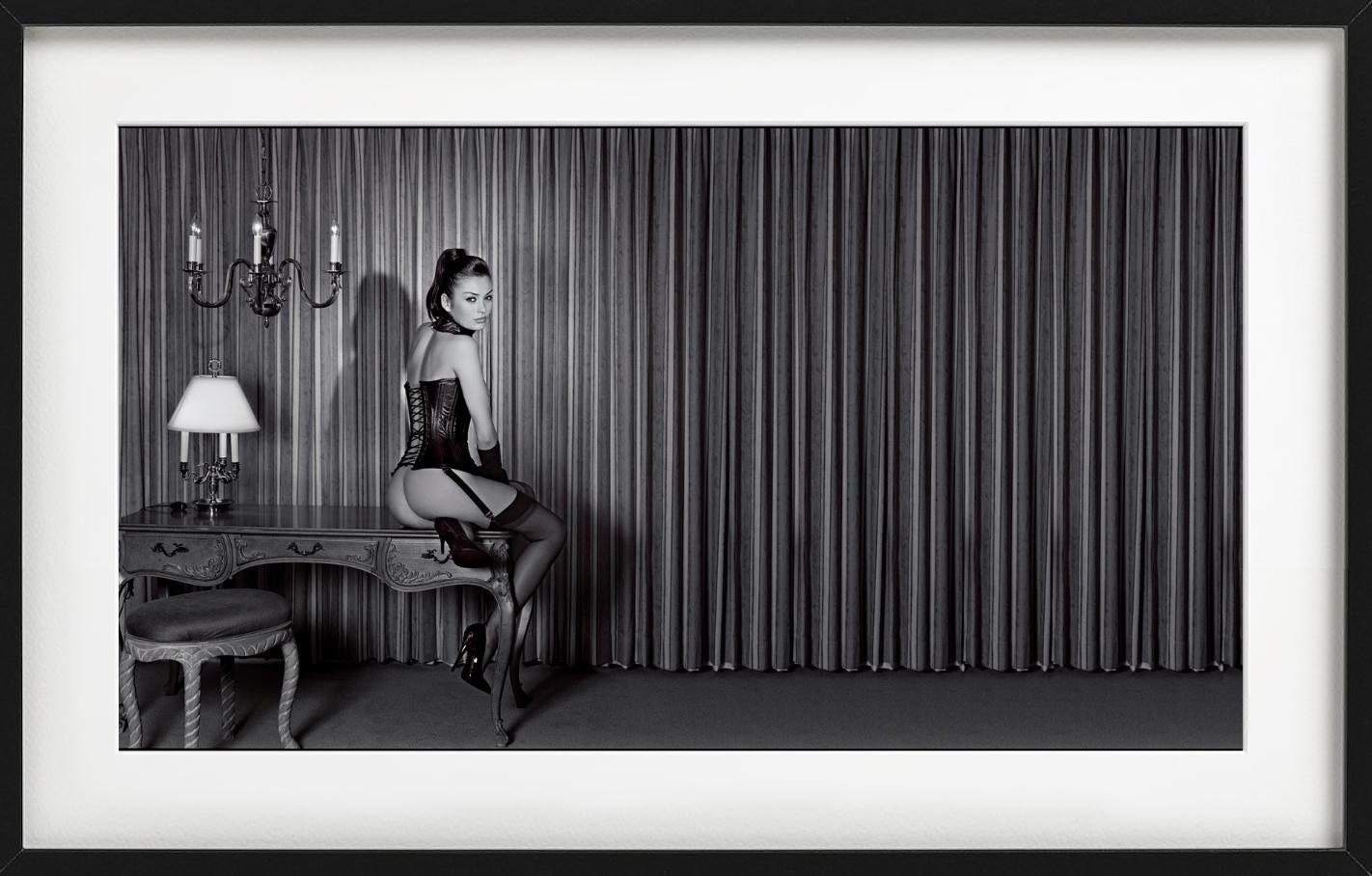 Petra dans un corset en cuir, mannequin assis sur un bureau ancien, photographie d'art - Photograph de Guido Argentini