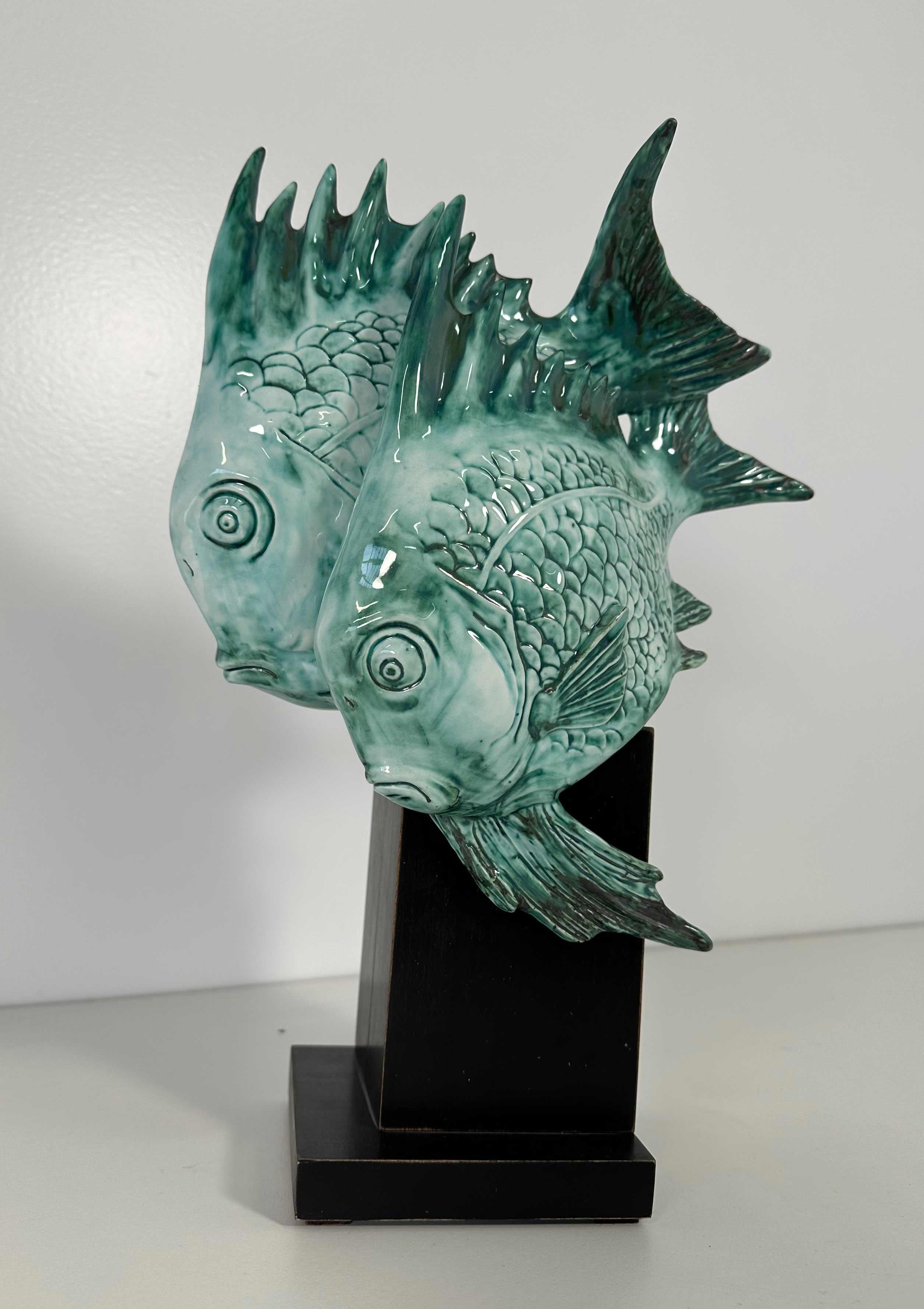 Cette sculpture Art déco a été produite en Italie, et plus précisément à Milan, par Guido Cacciapuoti dans les années 1930. 

La base est en bois ébonisé et la sculpture, un couple de poissons, est en grès cérame bleu clair.

Sous la base se