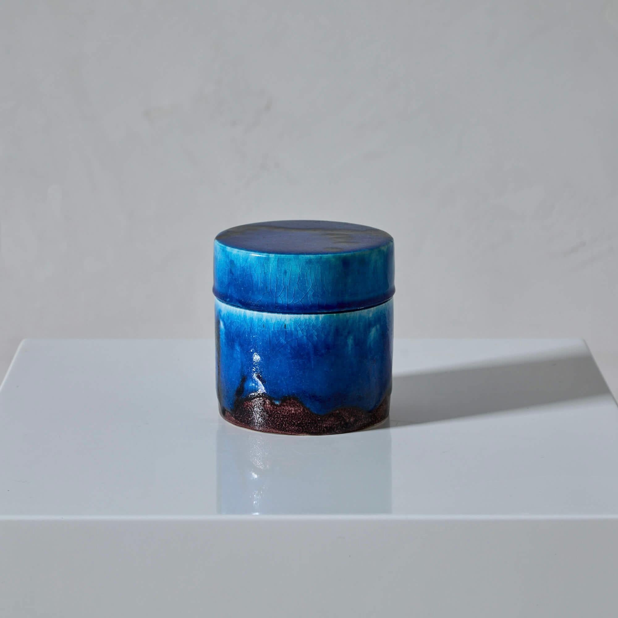 Questa scatola di ceramica ha uno smalto vivace che si estende a cascata sulla superficie, raccogliendosi verso la base per rivelare un bordo strutturato. All'interno, la scatola è smaltata di bianco e offre un contrasto sorprendente con l'esterno.
