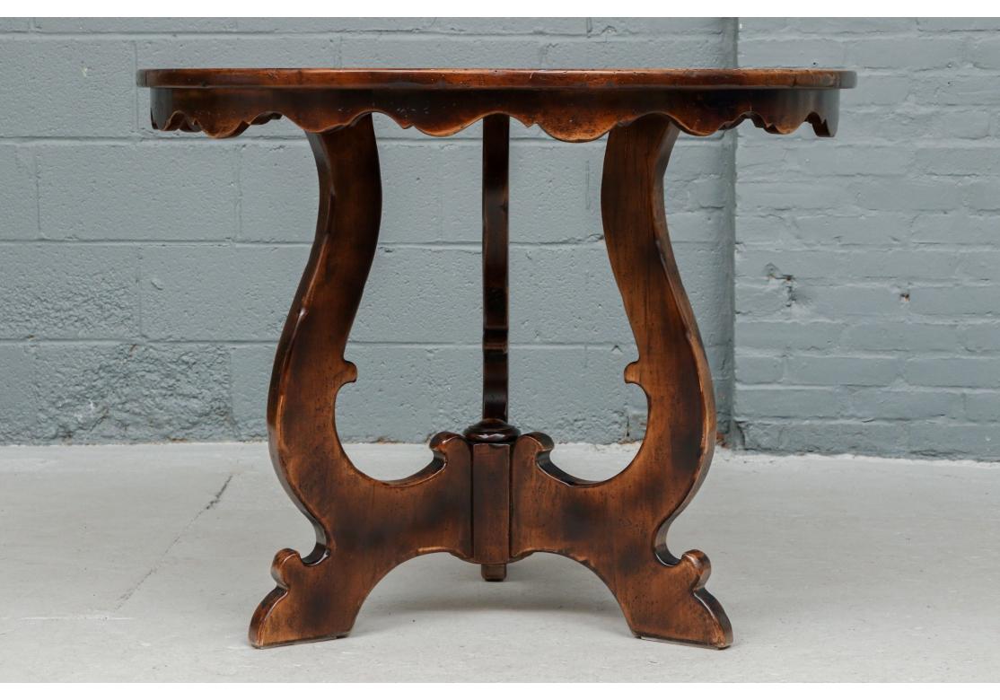 A well made and stylish table comprised of solid maple and walnut veneers In an antiqued dark stained finish. With a scalloped apron raised on a shaped tripod base. Made by Guido Zichele in Italy expressly for Bloomingdales. Bears label on