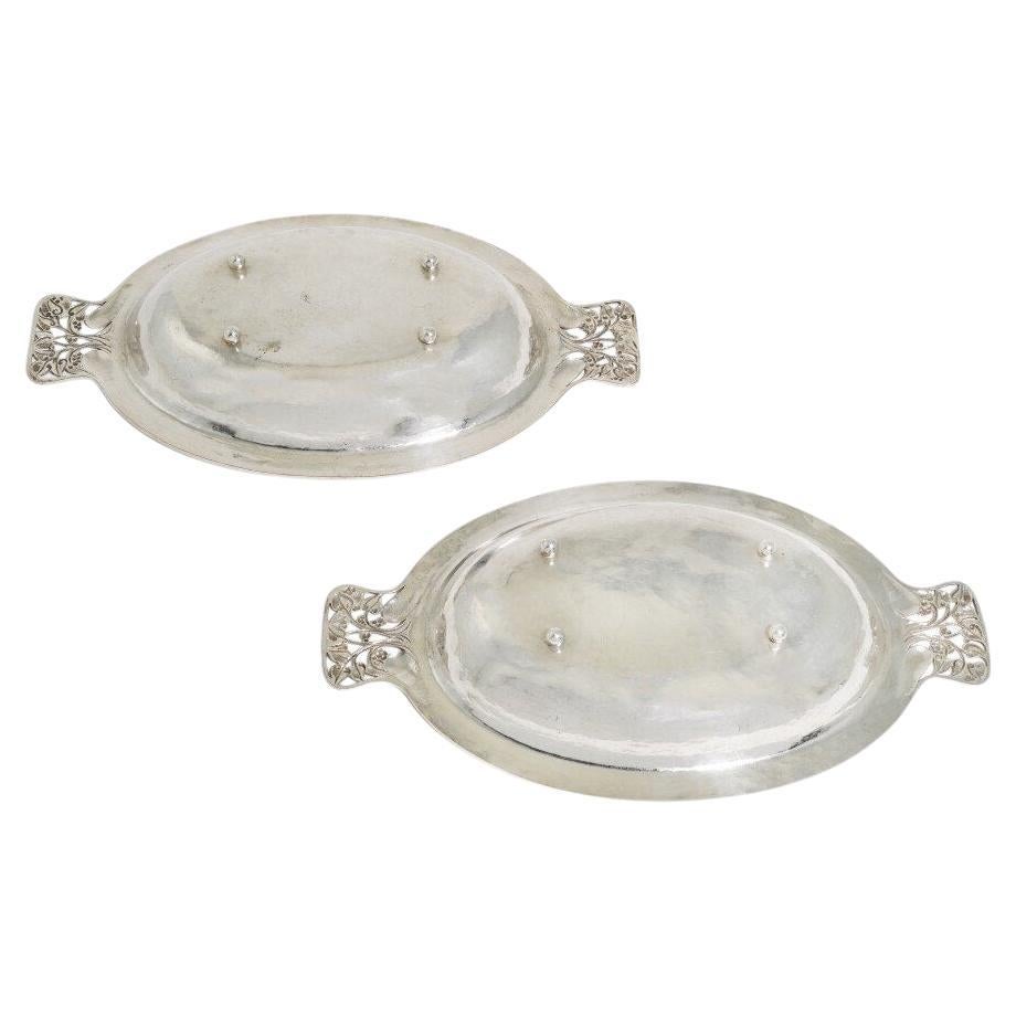 Guild of Handicraft, zugeschrieben. Ein Paar versilberte Gemüseschalen und Deckel, entworfen von C. R. Ashbee, um 1900. Ovale Form mit elfenbeinernen Endstücken, die mit Kettengliedern an blattförmigen Vorsprüngen befestigt sind. Die durchbrochenen