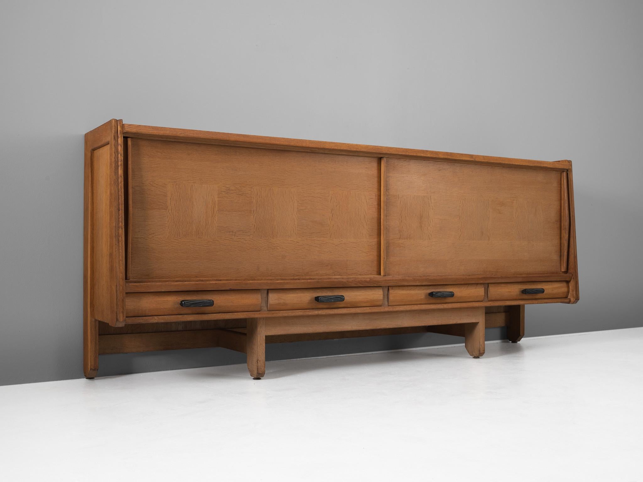 Guillerme & Chambron, credenza, oak, France, 1960s. 

Medium-sized sideboard with two sliding doors by French designer duo Guillerme and Chambron. This quite solid cabinet holds beautiful inlaid woodwork. Underneath the sliding doors there are