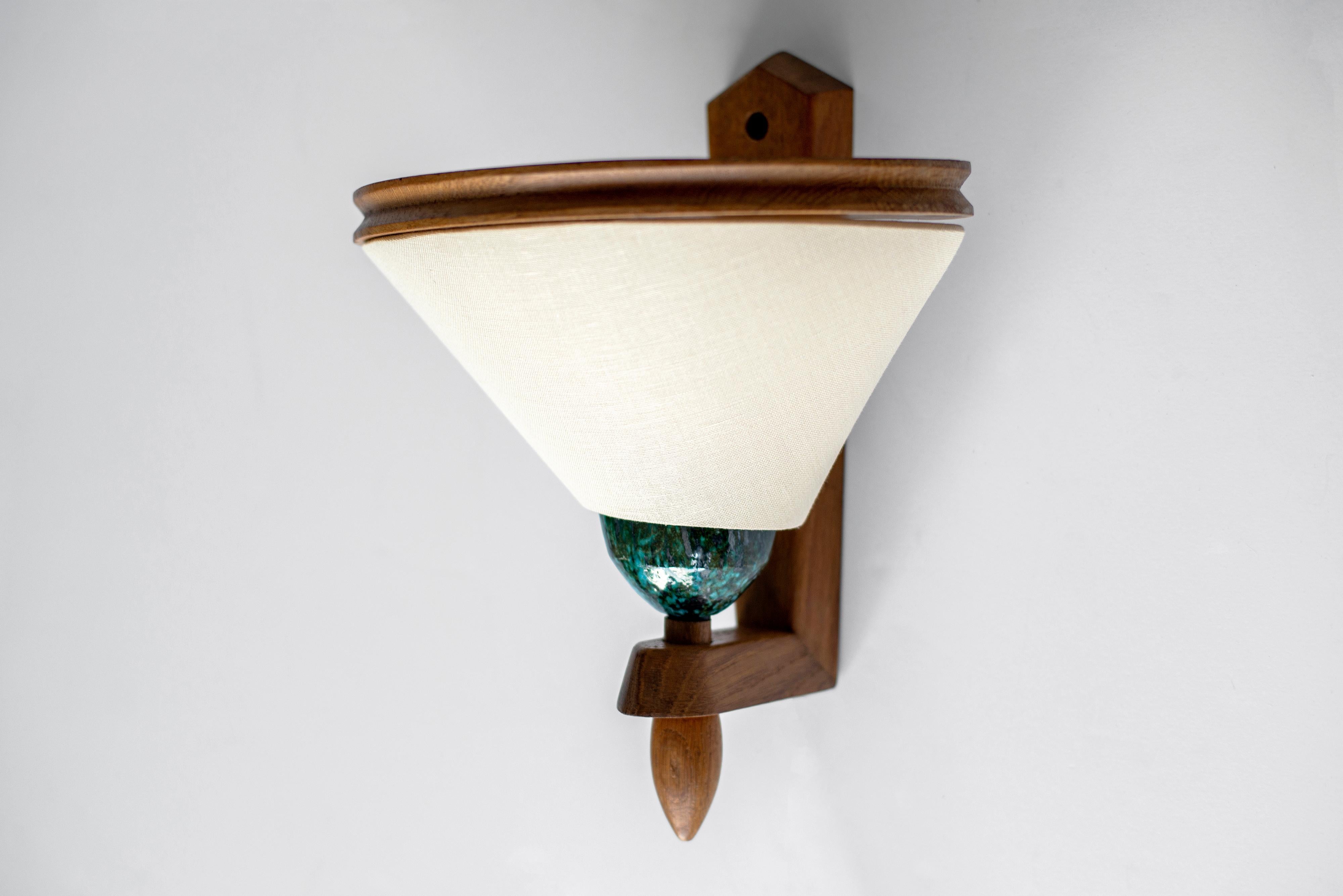 French wall sconce in French oak by Guillerme et Chambron.
Signature teal blue ceramic base with unique design wood ring meeting the new trapezoid shaped shade.
Professionally newly rewired.