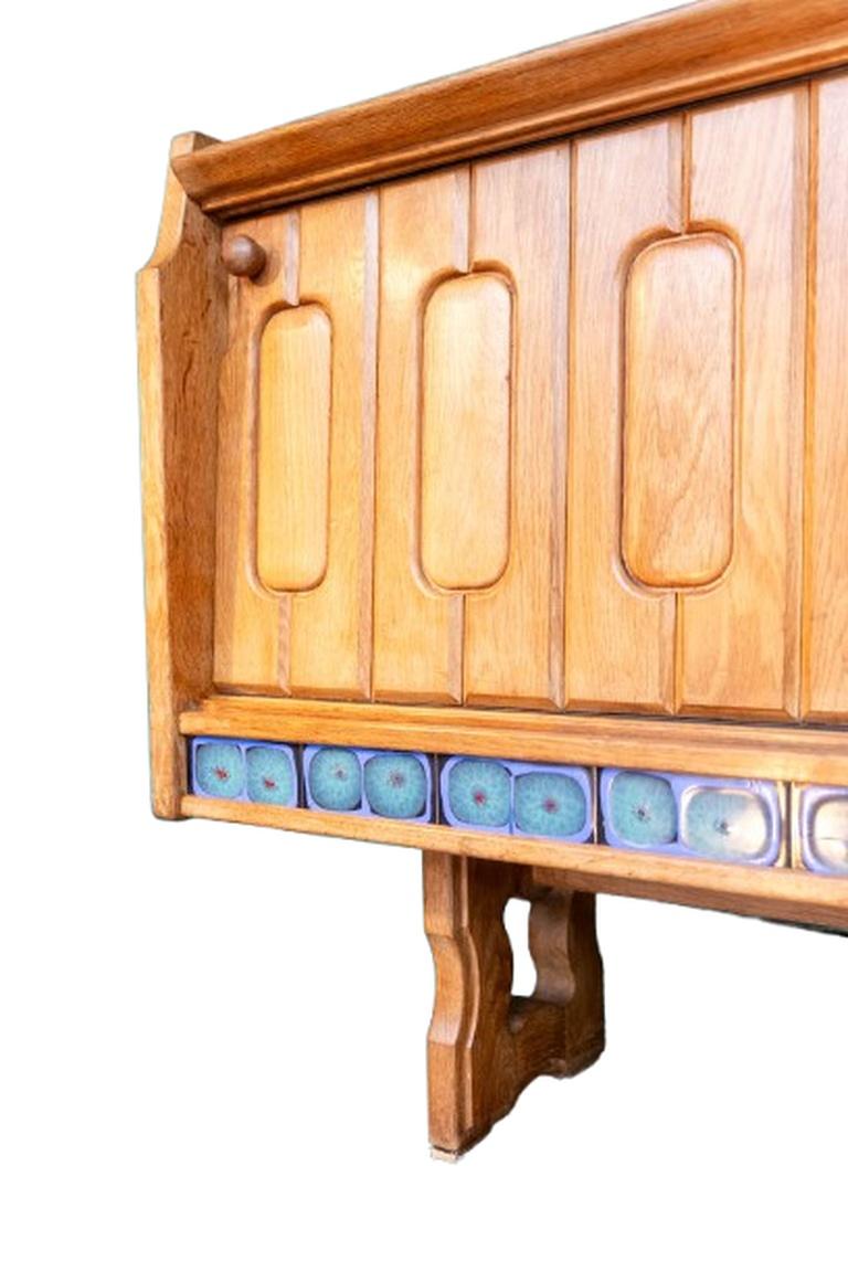 Guillerme and Chambron
Solid blond oak sideboard with two carved sliding doors and four small drawers. Decorated with ceramic tiles in a frieze on the front and top of the drawer section, probably the work of ceramicist Boleslaw Danikowski. The