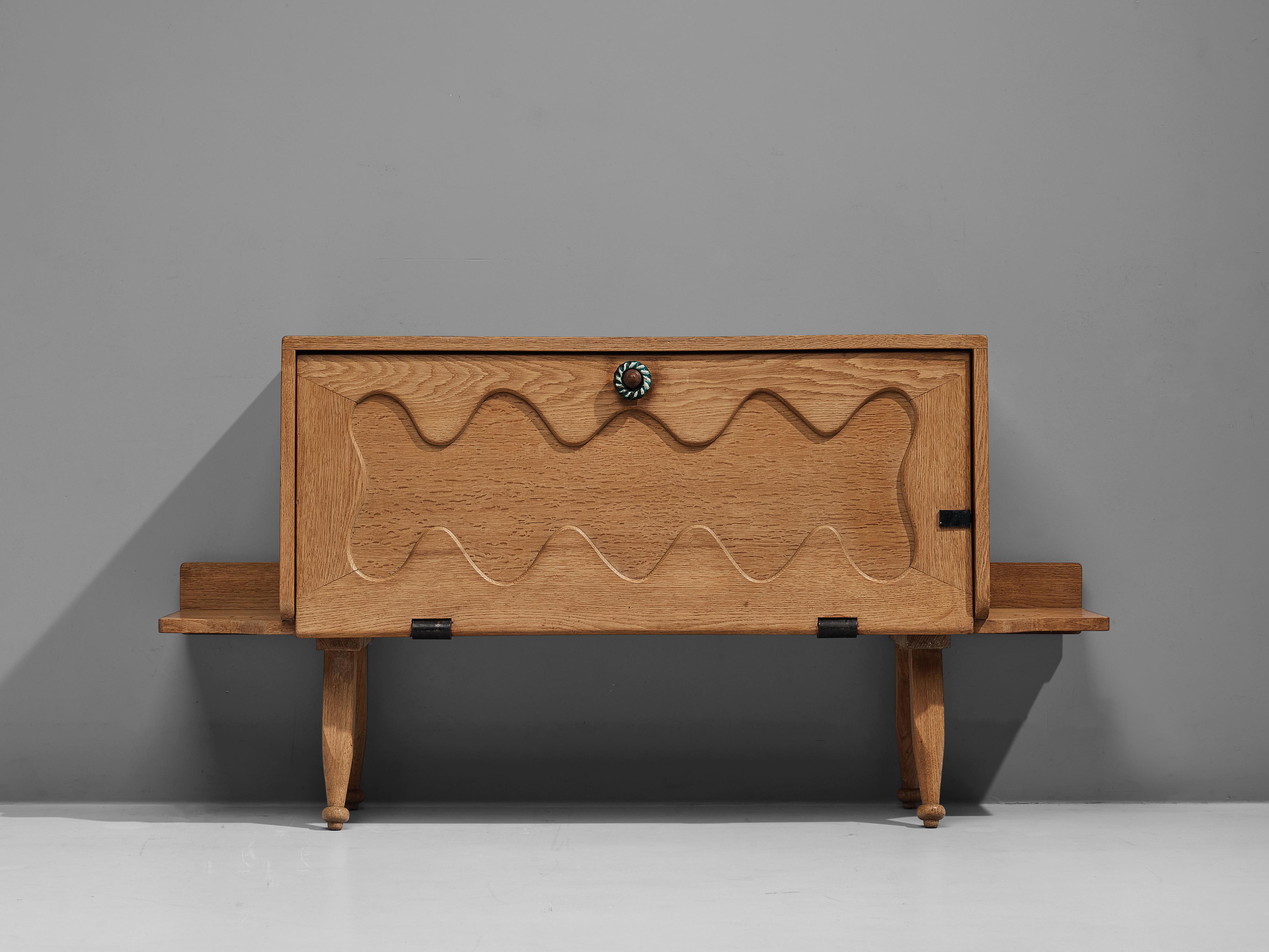 Guillerme & Chambron, sideboard with dry bar, oak, ceramic, France, 1960s

This charming sideboard is made by the designer duo Guillerme & Chambron. This item is a good example of excellent woodworking by virtue of the graphical designed door