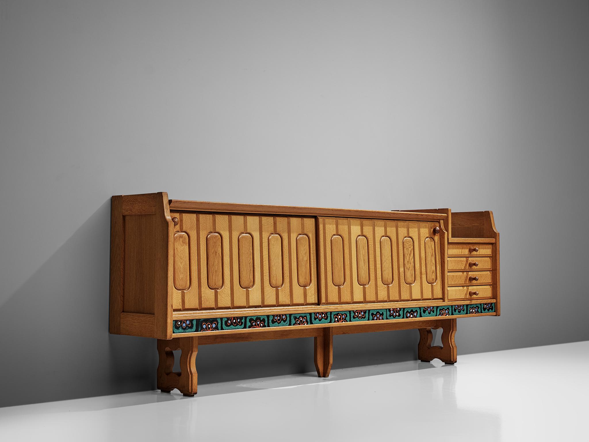 Guillerme et Chambron for Votre Maison, sideboard model Simon, oak and ceramic, France, 1960s.

Credenza in oak by French designers Guillerme & Chambron. This sideboard is equipped with two sliding-doors and a set of drawers. The front of the