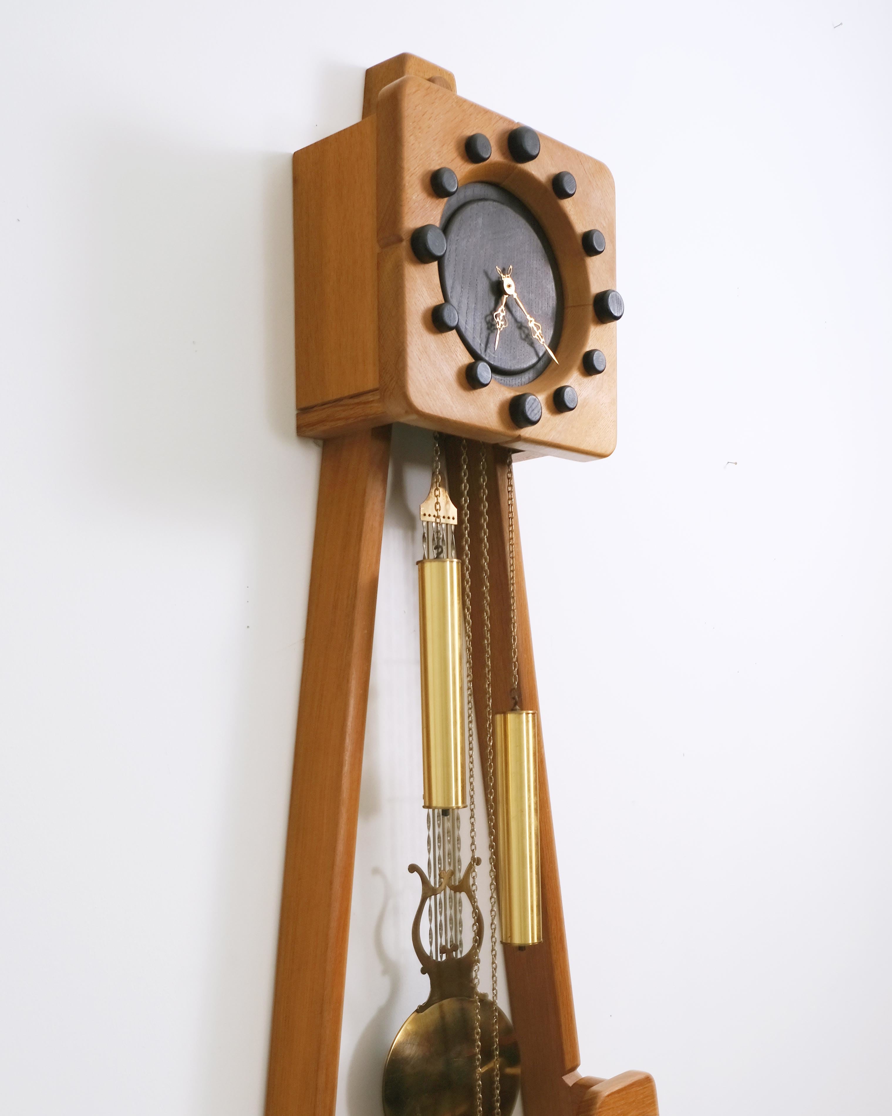 c. 1970s
Chêne clair et teinte noire, pendule et poids en laiton. 
H127 x W44 x D19 cm