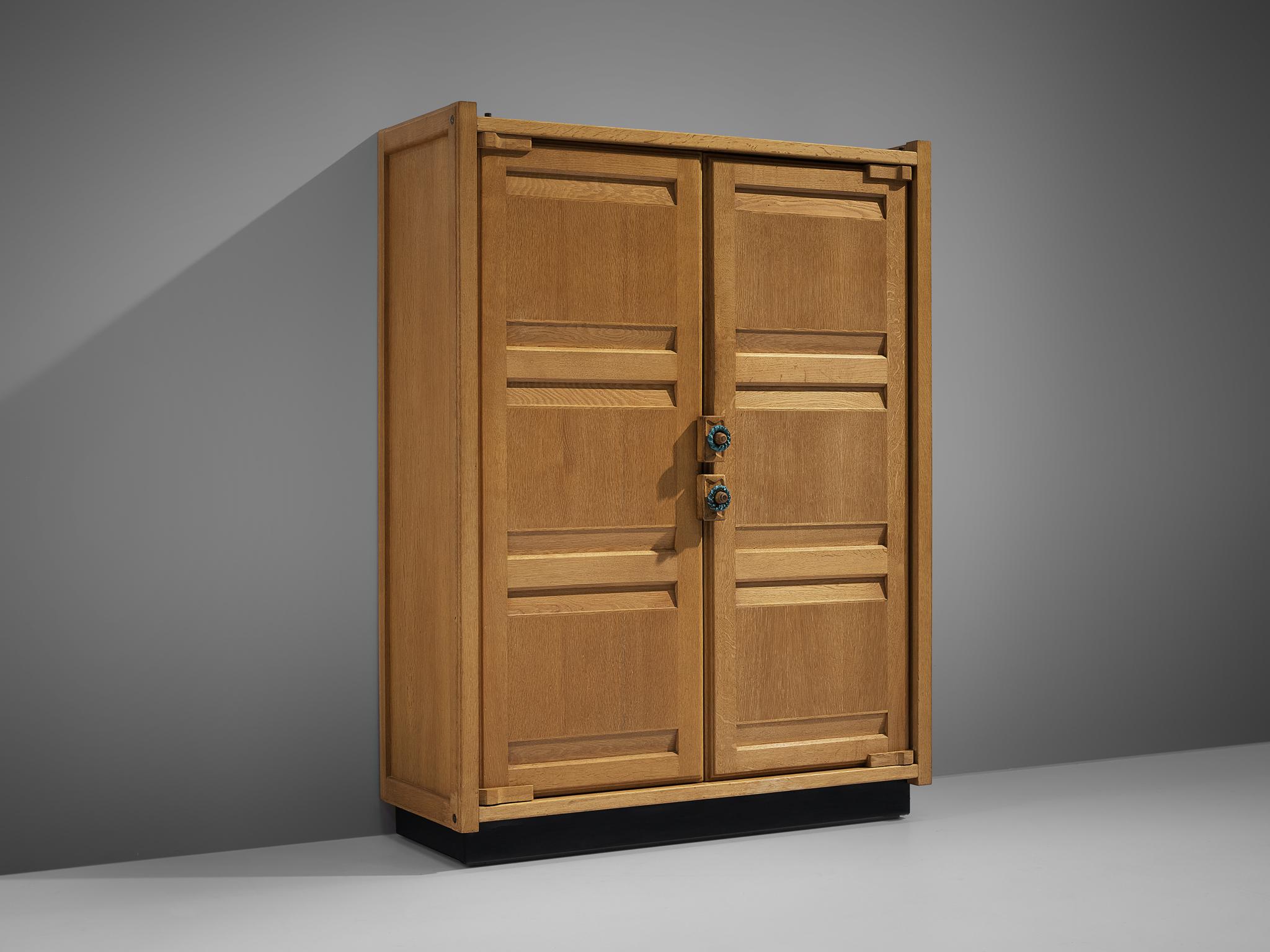 Guillerme et Chambron, armoire, oak, France, 1960s.

This case piece is designed by Guillerme and Chambron and features horizontal panels on the front. The armoire is equipped with colorful, ceramic handles. The cabinet features distinct sculptural