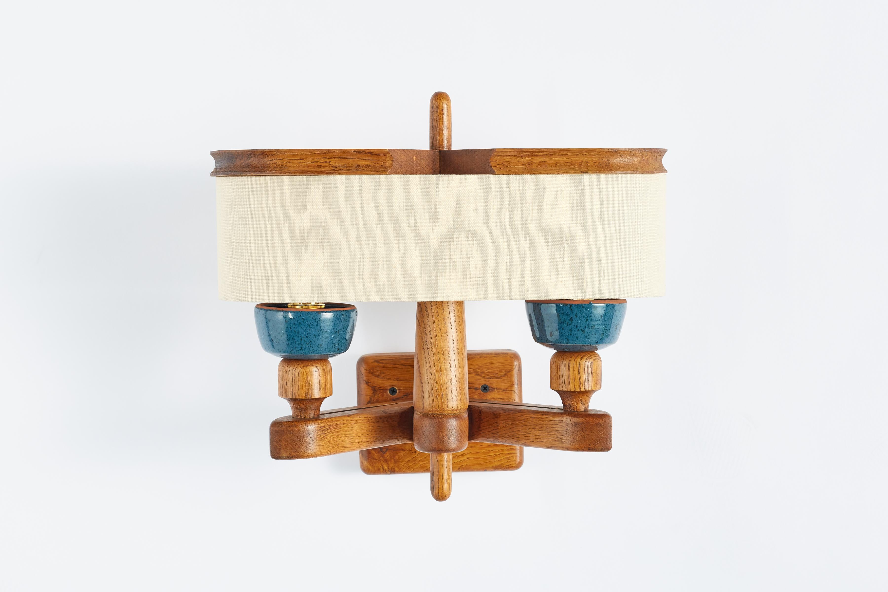 Rare wall sconce by Guillerme et Chambron - France, 1940's.

Blue ceramic sockets with signature oak frame and new single linen shade.

Rewired.