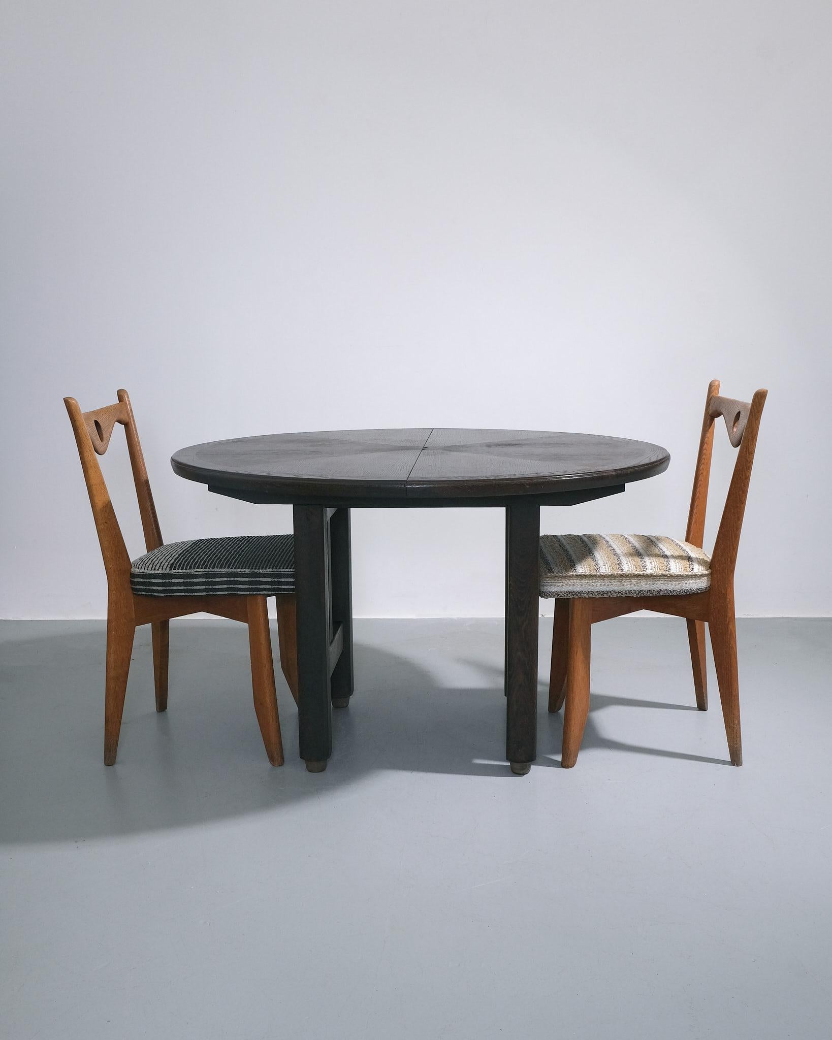 Table de salle à manger à rallonge de Guillerme et Chambron pour l'Edition Votre Maison, France, c.C.. La table présente un plateau circulaire en chêne ciré teinté noir avec des rallonges cachées qui coulissent sous la surface principale. La base