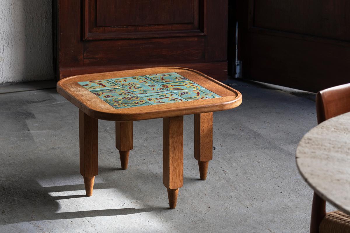 Coffee table designed by Guillerme et Chambron, produced in France in the 1970s. A solid oak wooden frame with characteristic square and conical ‘pencil’ legs. An inlay of figurative ceramic tiles with a depiction of all kinds of abstract faces. The