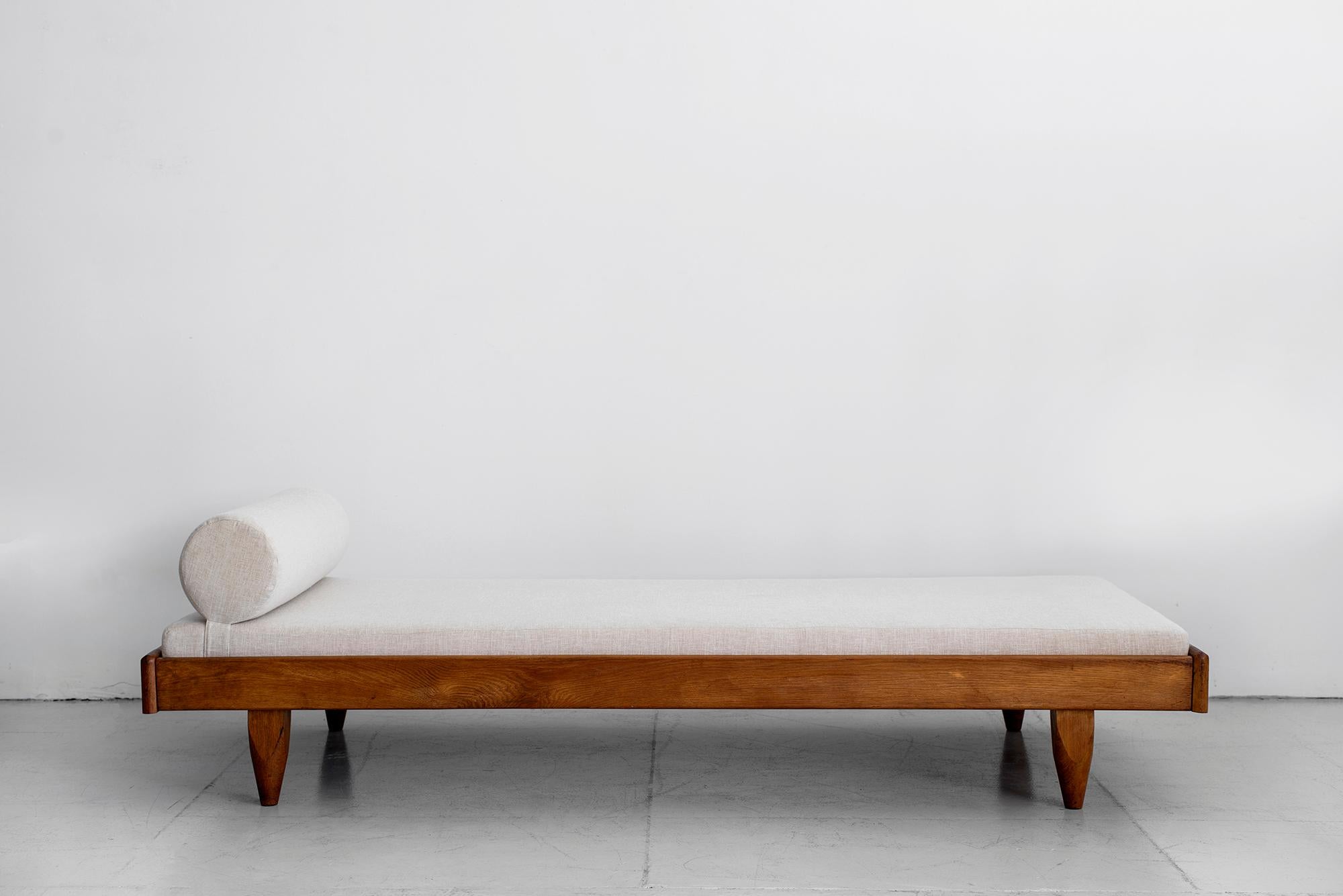 Stunning and rare French daybed by Guillerme et Chambron. Oak base with newly upholstered linen cushion and adjustable bolster pillow. Great patina and coloring to wood.