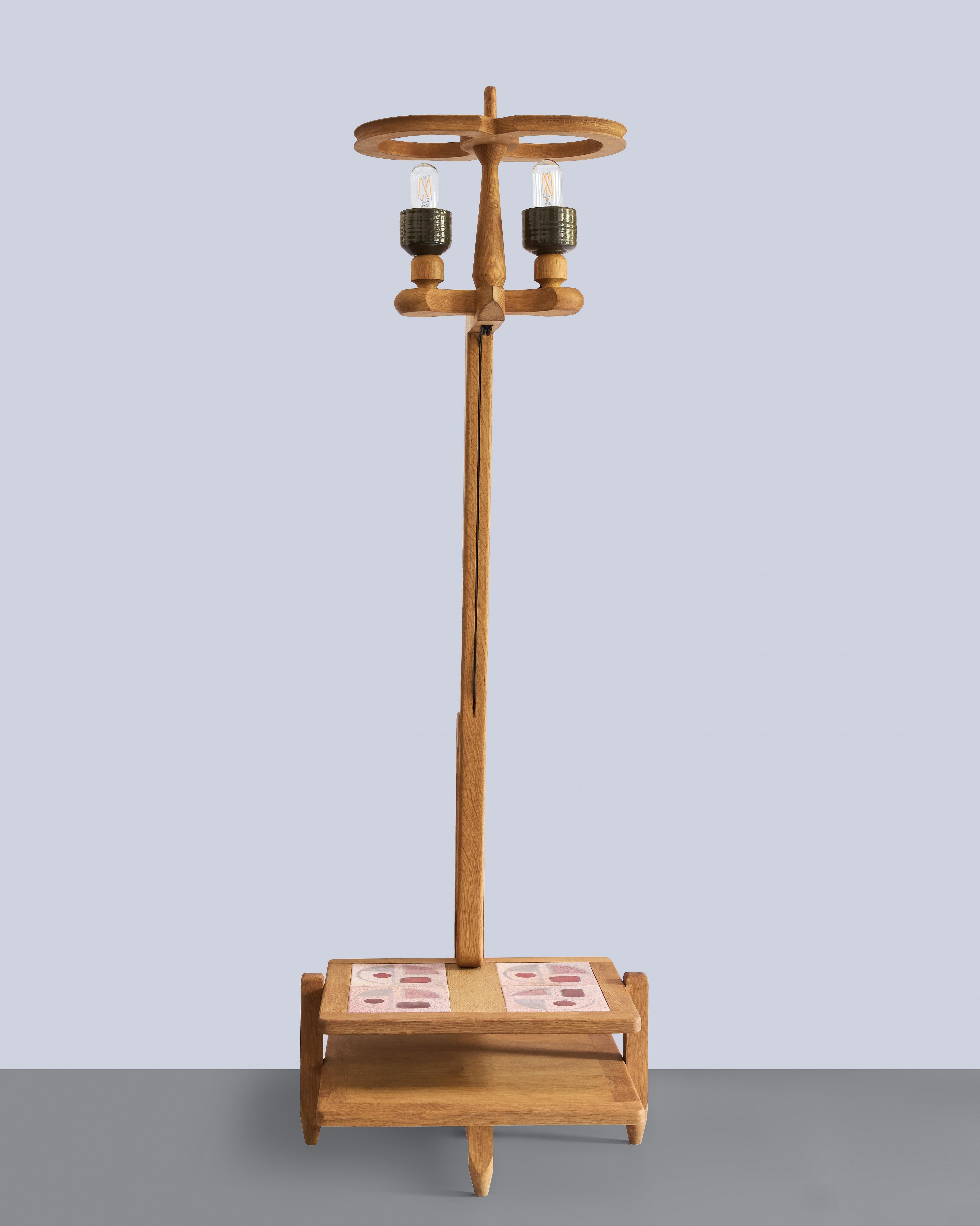 Ce lampadaire de Guillerme et Chambron pour l'Edition Votre Maison, datant des années 1960, est fabriqué en chêne ciré avec des détails en carreaux de céramique. Le design combine l'éclairage avec des étagères intégrées, avec deux niveaux bas, l'un