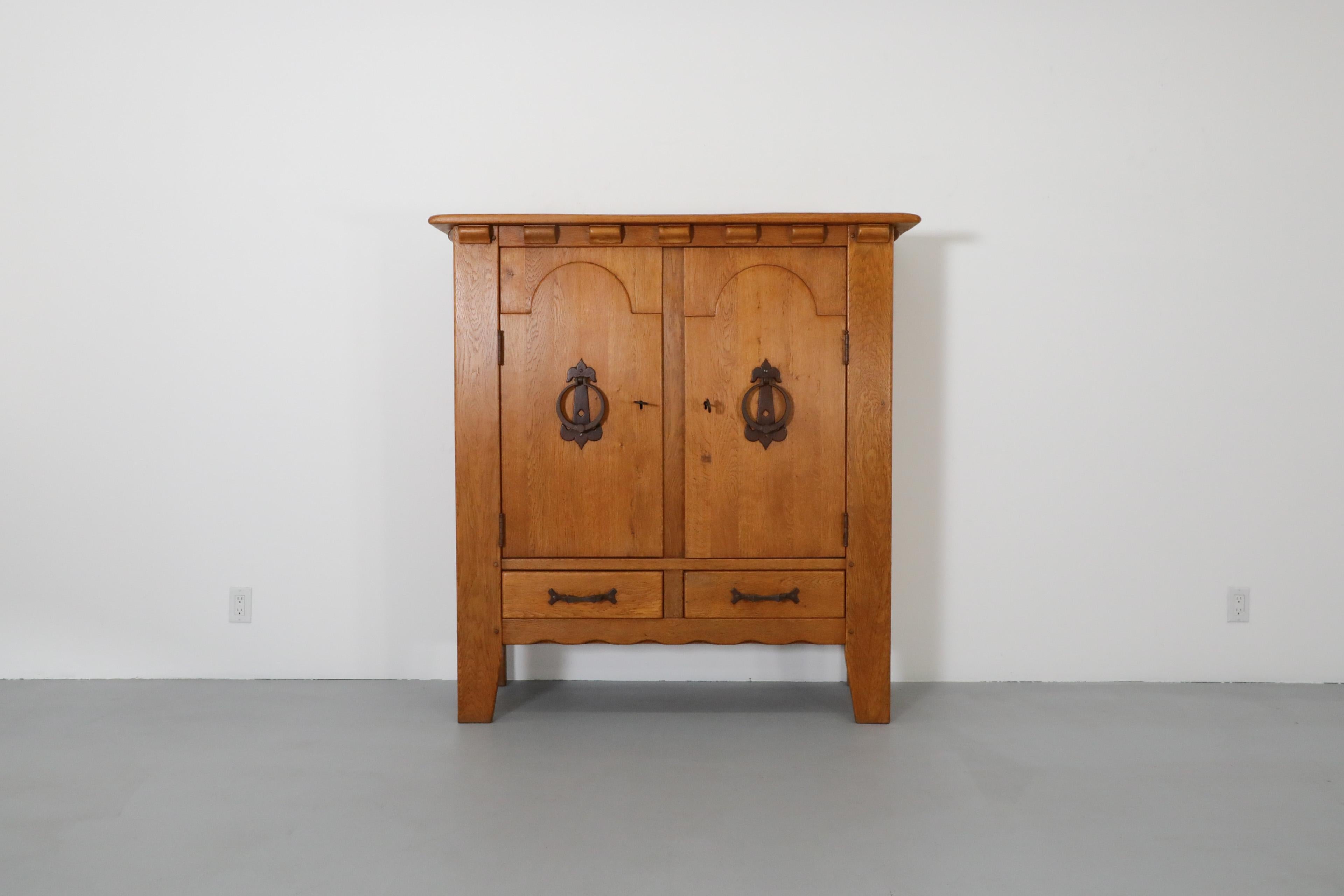 Mid-Century Guillerme et Chambron Inspired solid oak sideboard by Sprij Meubelen. This large, high sideboard has two doors concealing two sizable storage spaces above two pull-out lower drawers for additional storage. The decoratively carved oak is