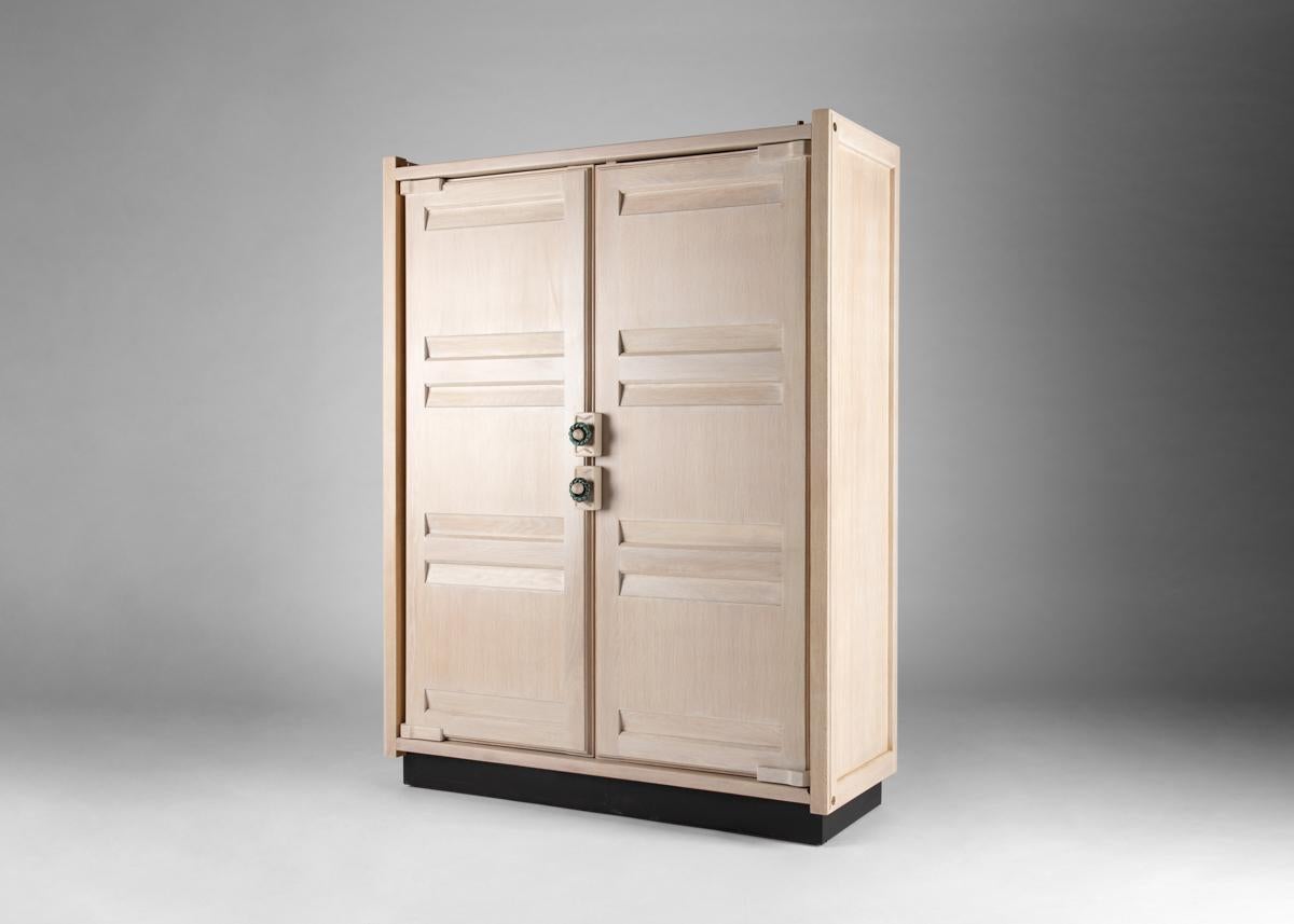 Cette armoire à deux portes en chêne chaulé, datant du milieu du siècle dernier, a été créée par le célèbre designer français Robert Guillerme dans le cadre d'une ligne de design qu'il a produite pour la société Votre Maison. Poignées exécutées par