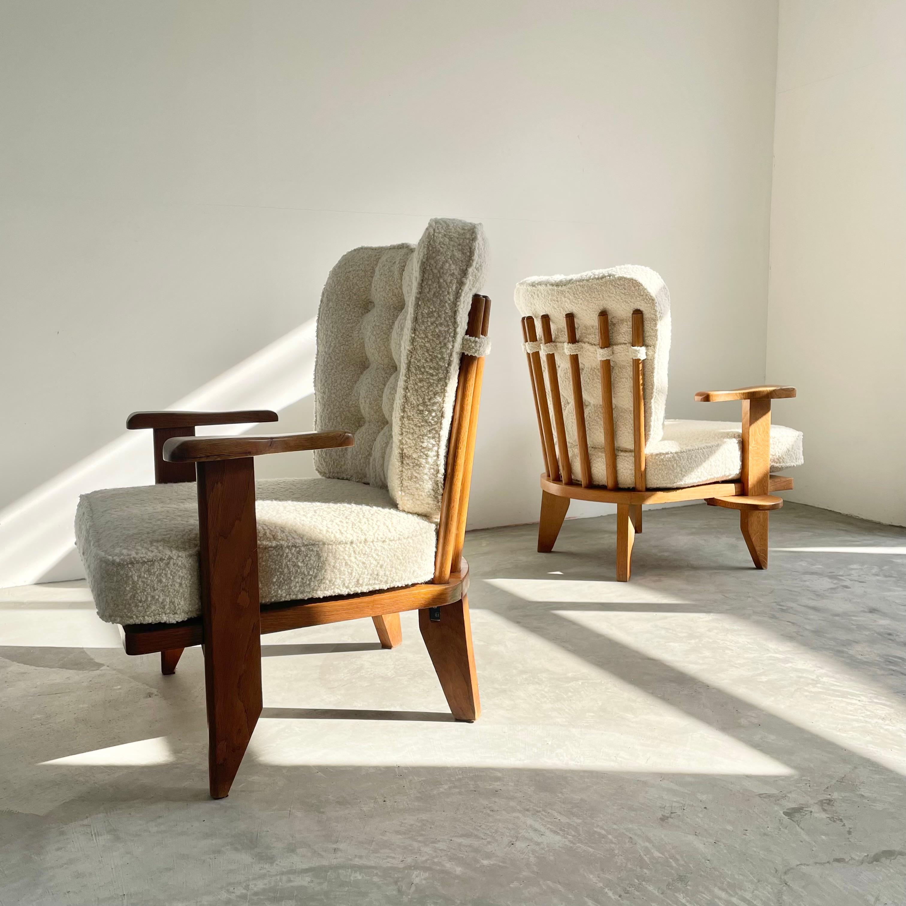 Gorgeous pair of Guillerme et Chambron Oak Armchairs with a plush cream Boucle upholstery. Edition Votre Maison. Each chair has a small slide out side table that pivots out under the right side of the seat which you can pull out and use for drinks,