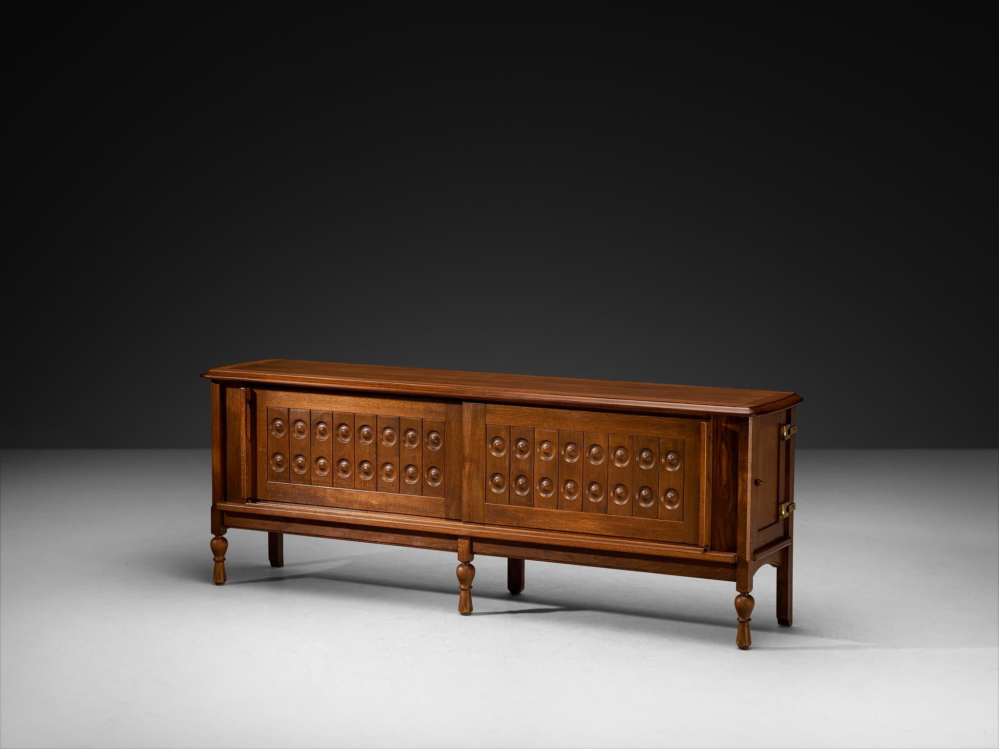 Guillerme et Chambron per Votre Maison, credenza, Oak, ottone, Francia, anni '60 

Questa credenza in rovere massiccio, disegnata da Guillerme et Chambron, riflette la caratteristica sintesi di dettagli scultorei e rigore funzionale del duo. La