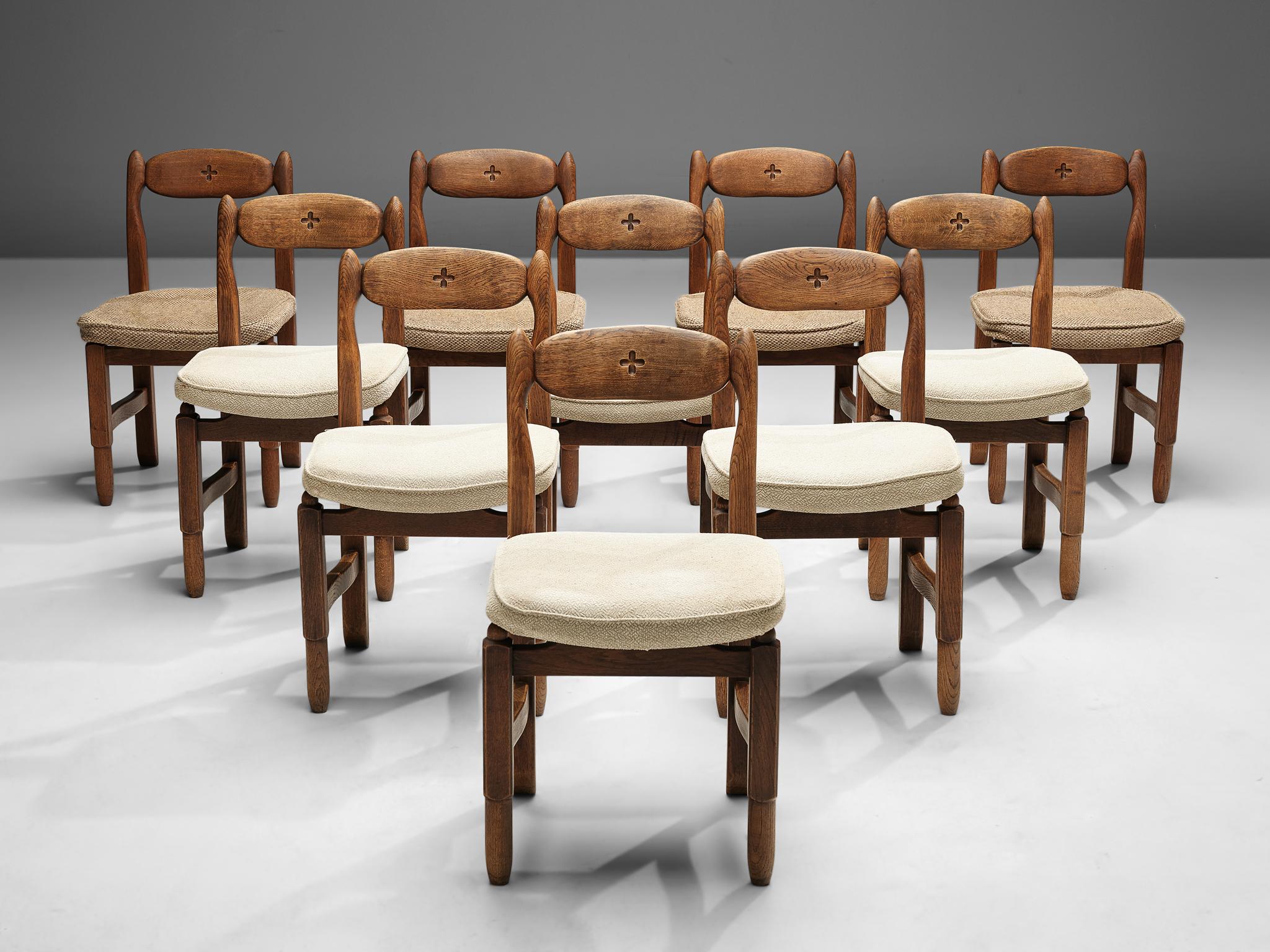 Guillerme et Chambron, set of ten ‘Lorraine’ dining chairs, oak, fabric upholstery, France, 1960s.
 
This set of ‘Lorraine’ dining chairs by French designer duo Guillerme et Chambron shows a decorative motif in the backrest. Here a cross with four