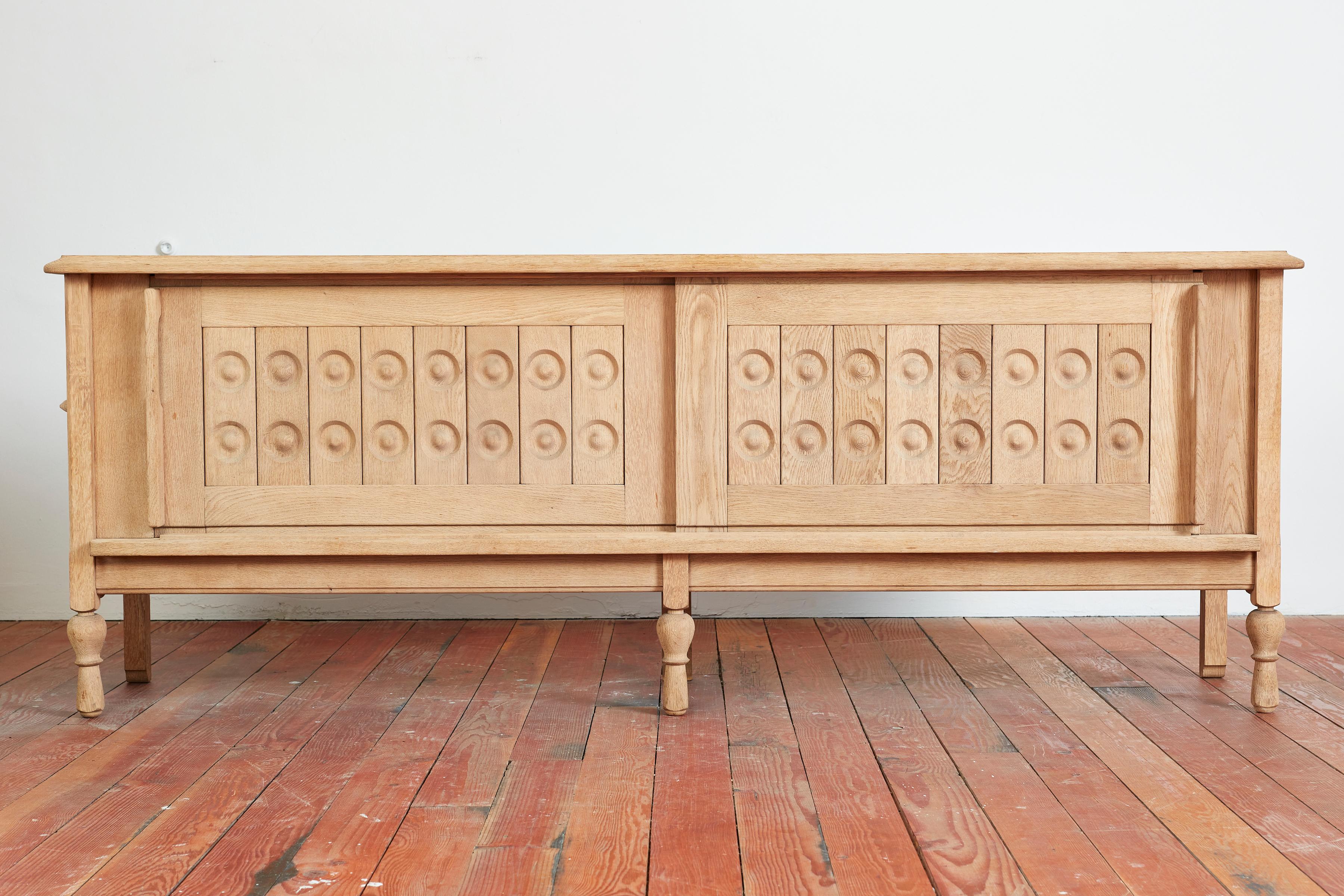 Beautiful sideboard by Guillerme et Chambron - France, 1950s
Carved sliding doors with circular patterned etchings on door fronts
Open shelving interiors 
Extra secret storage on both ends with hinged door with brass hardware
Carved legs