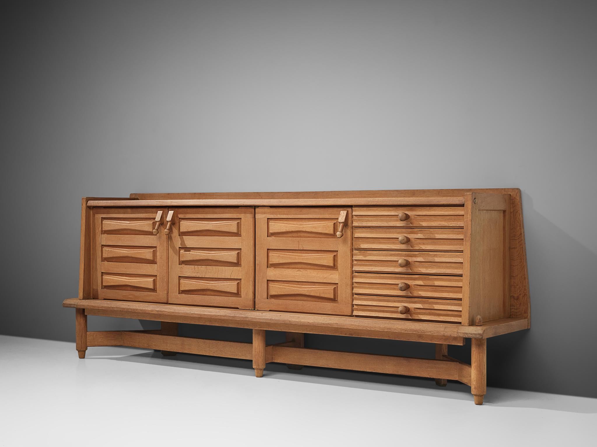 Guillerme et Chambron, large sideboard in oak, France, 1960s.

This large sideboard is designed by the company Guillerme et Chambron. It features a geometric structure on the front side, with protruding door handles on the top of the doors. Behind