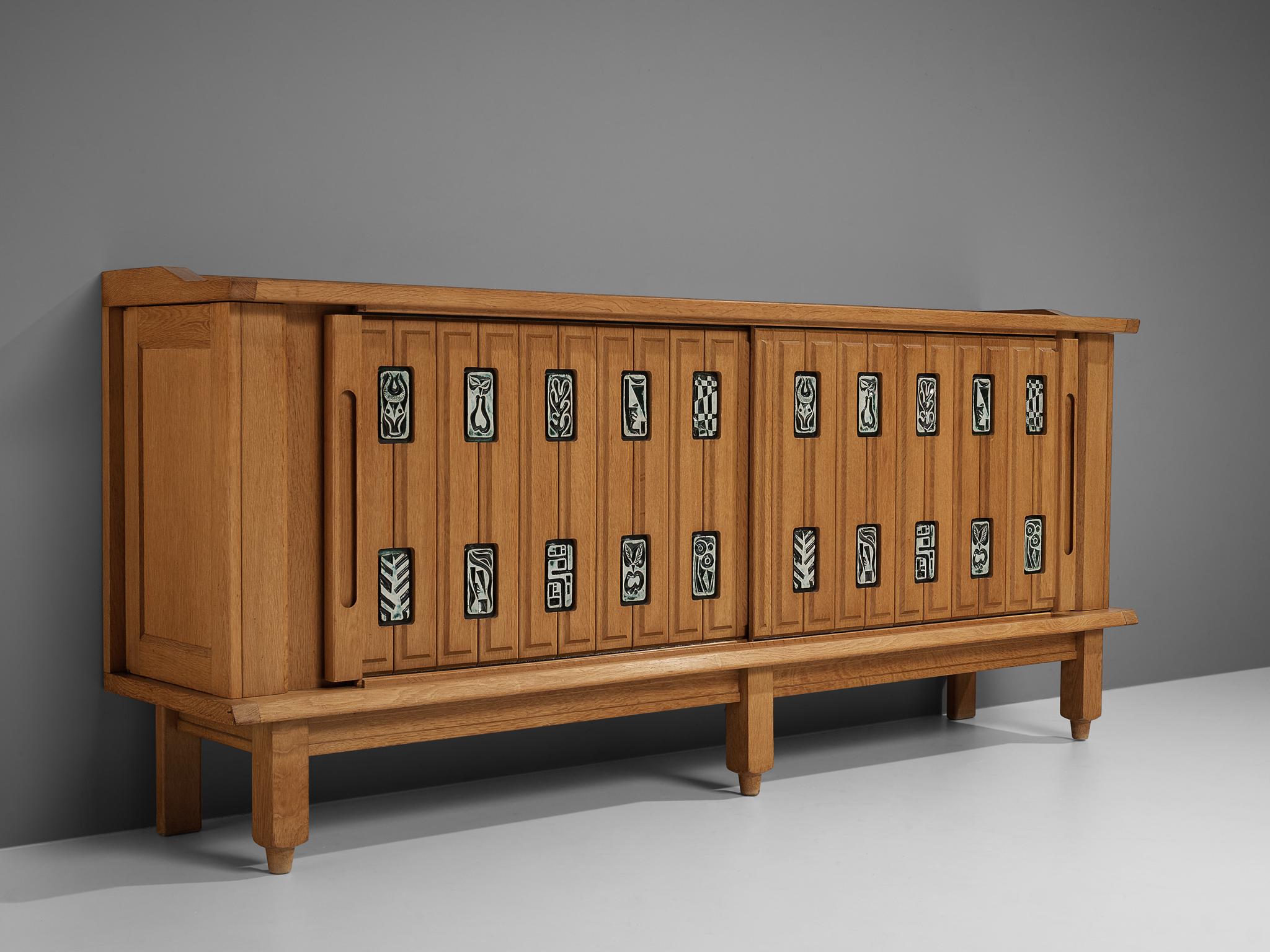 Guillerme et Chambron, sideboard, oak, ceramics, France, 1950s

This sculptural cabinet is executed in oak with ceramic detailing. The sideboard features two sliding front doors as well as two pullout / pull-out doors on the sides that provide