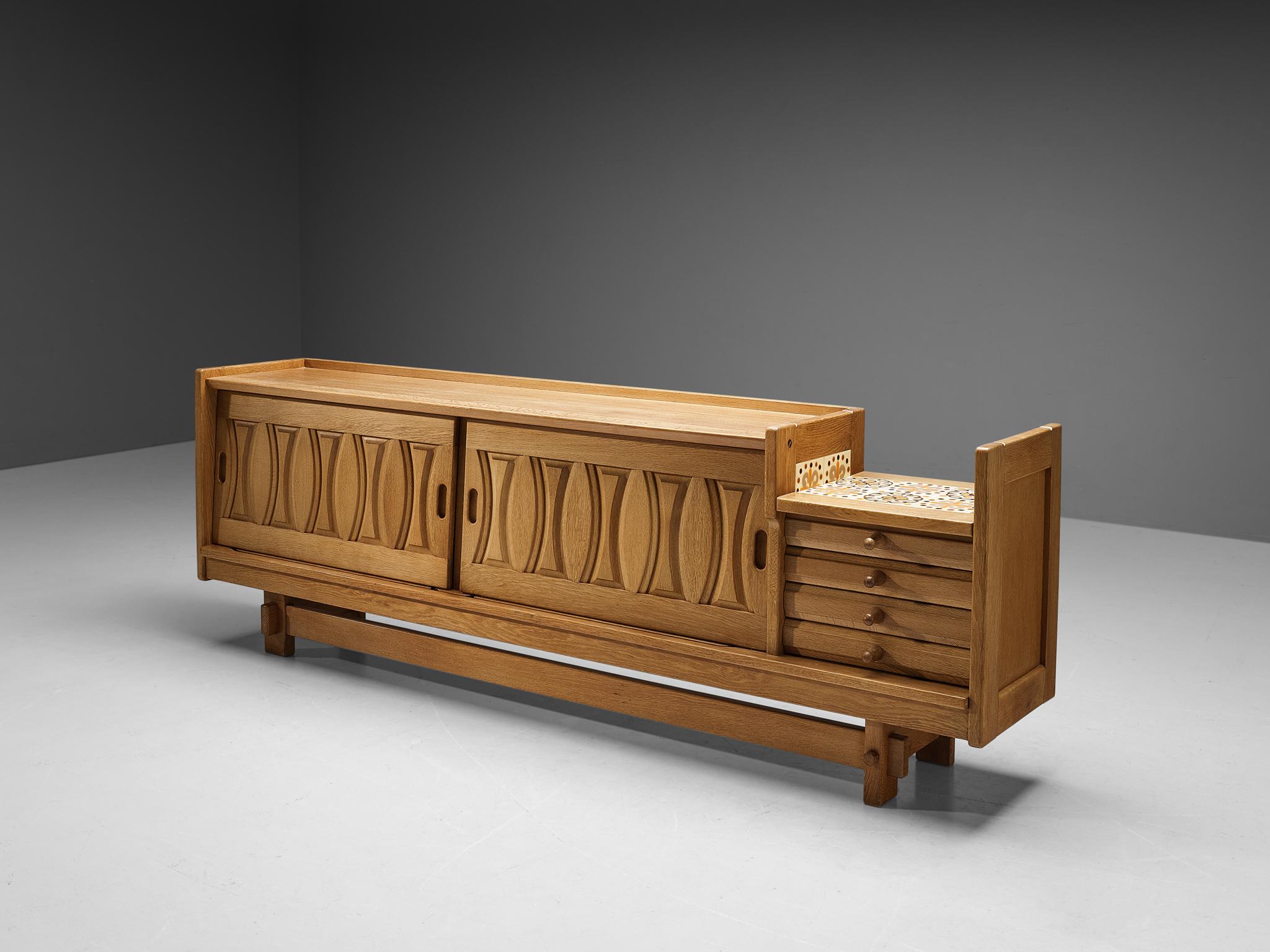 Guillerme et Chambron for Votre Maison, sideboard, oak, ceramics, France, 1960s.

Credenza in oak by French designers Guillerme & Chambron. This sideboard is equipped with two sliding doors and a set of four drawers. The front of the sideboard is