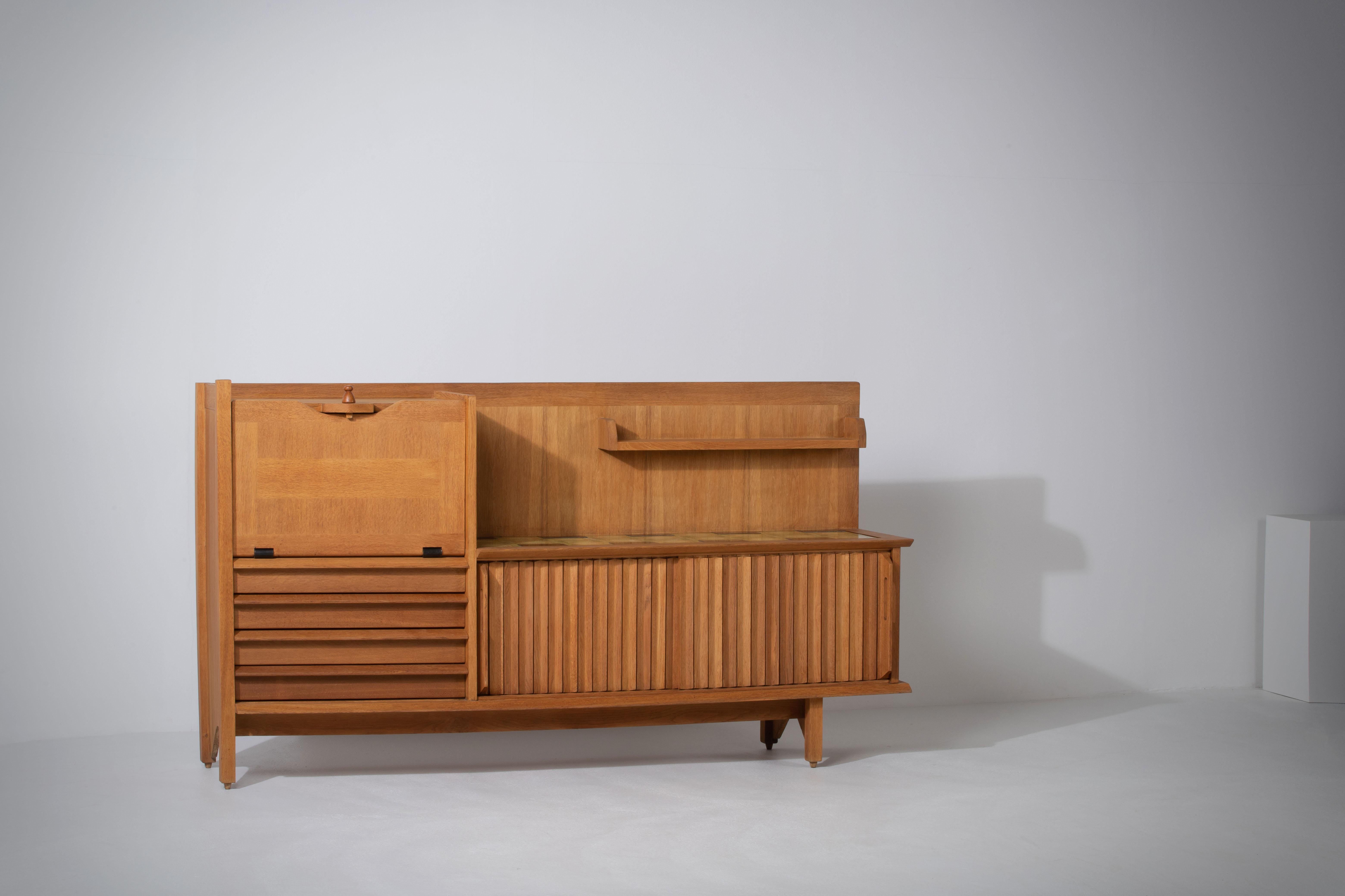 This characteristic cabinet, buffet in solid oak is designed by the French designer duo Jacques Chambron (1914-2001) and Robert Guillerme (1913-1990). It features two sliding front doors, one pullout door on the left side and four drawers that