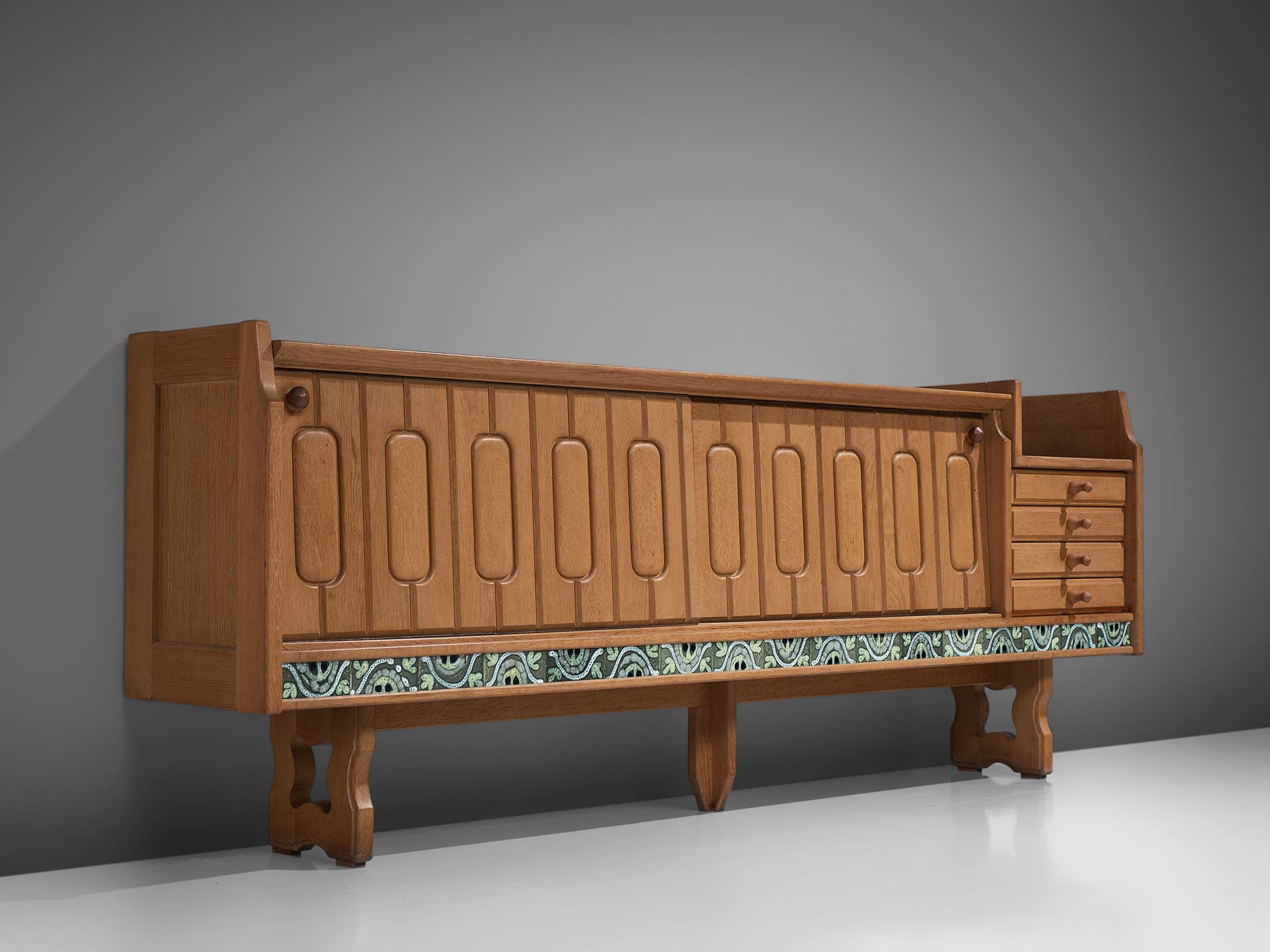 Guillerme et Chambron, Sideboard model Simon, oak and ceramic, France, 1960s. 

Credenza in oak by French designers Guillerme & Chambron. This sideboard is equipped with two sliding-doors and a set of drawers. The front of the sideboard is